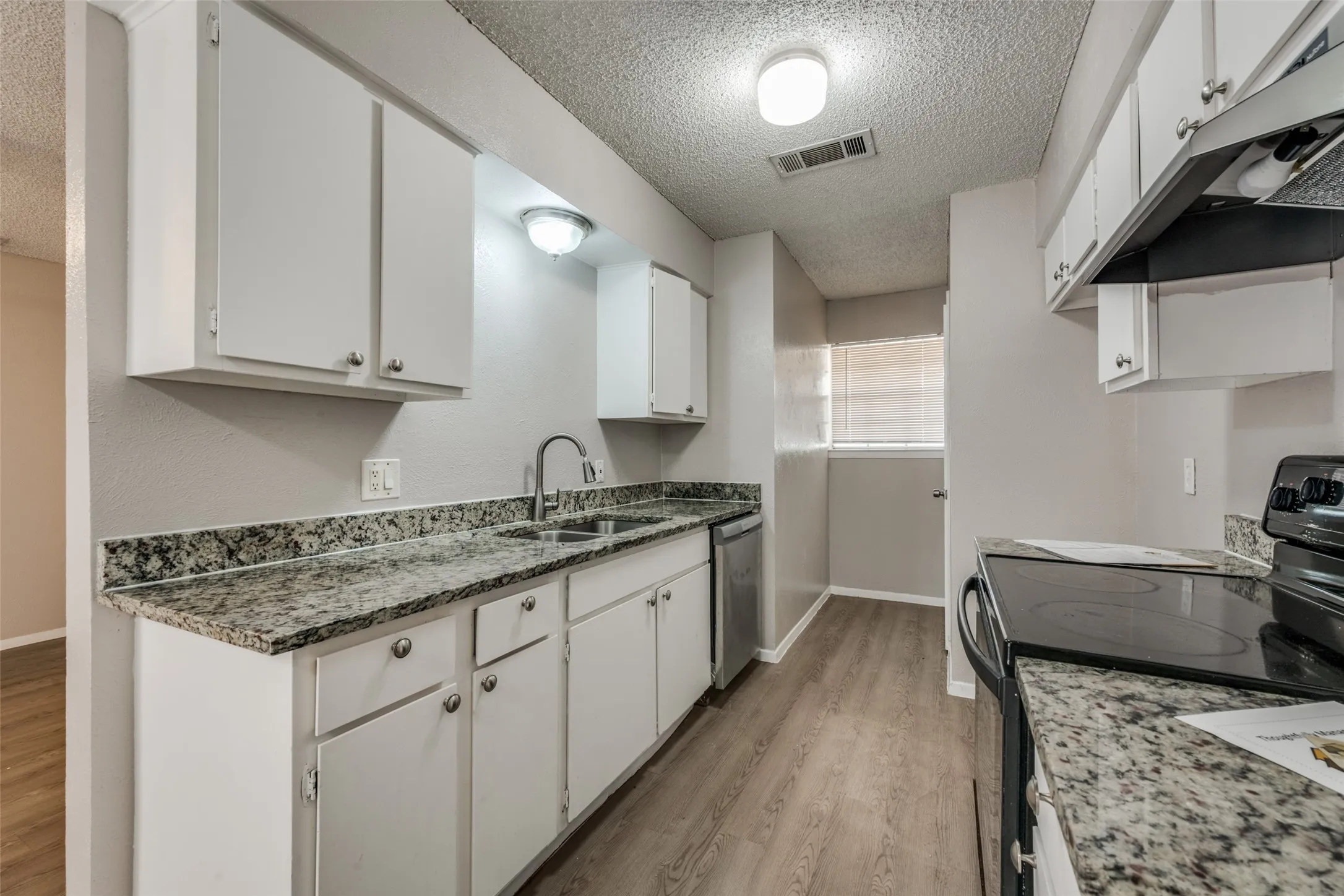 Kitchen featuring white cabinetry, granite-style countertops, wood-finish flooring, and a stainless steel dishwasher