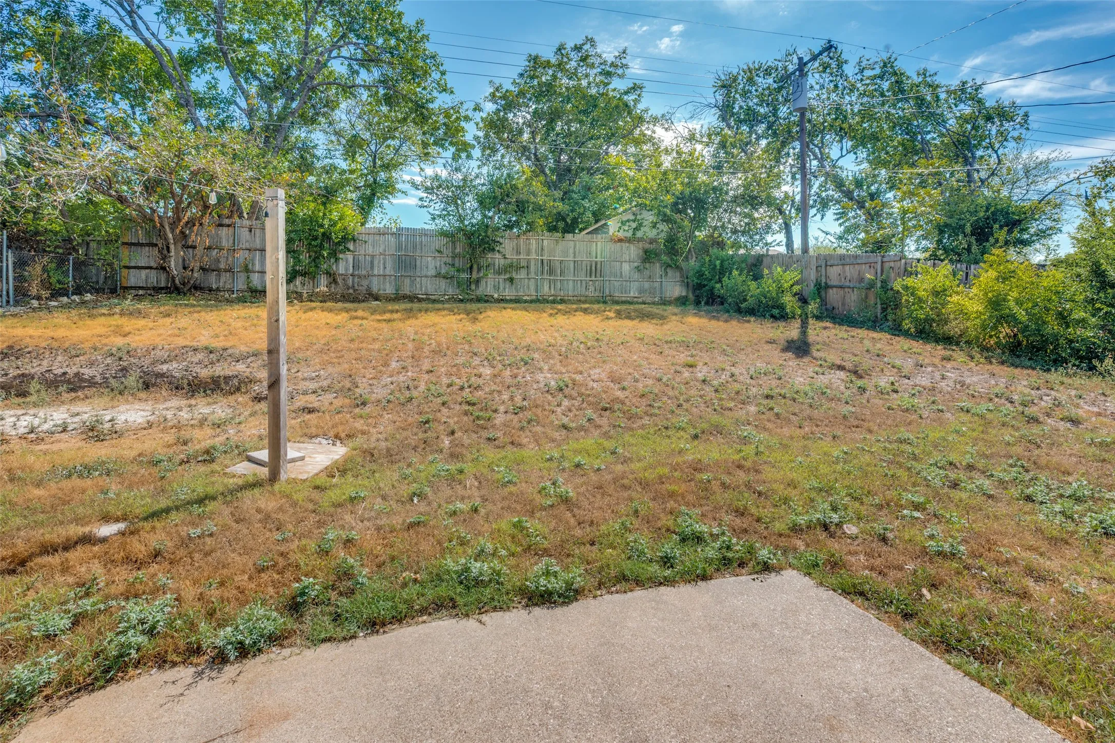 Expansive yard featuring a concrete patio, wood fencing, and mature trees