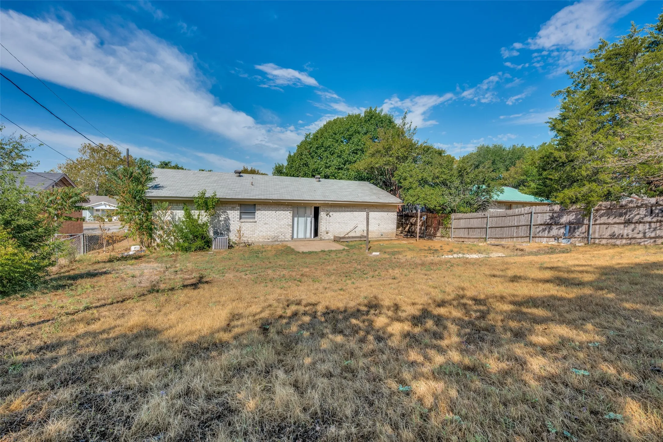 Expansive backyard featuring a wood privacy fence, mature trees, and a brick exterior with sliding glass doors
