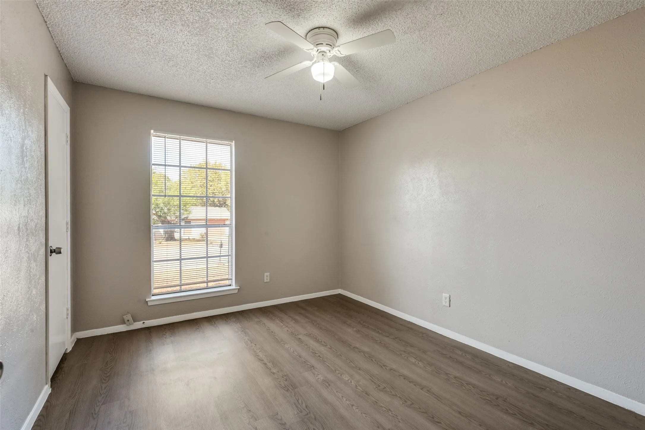 Spacious room featuring wood-finish flooring, a ceiling fan, and a large window