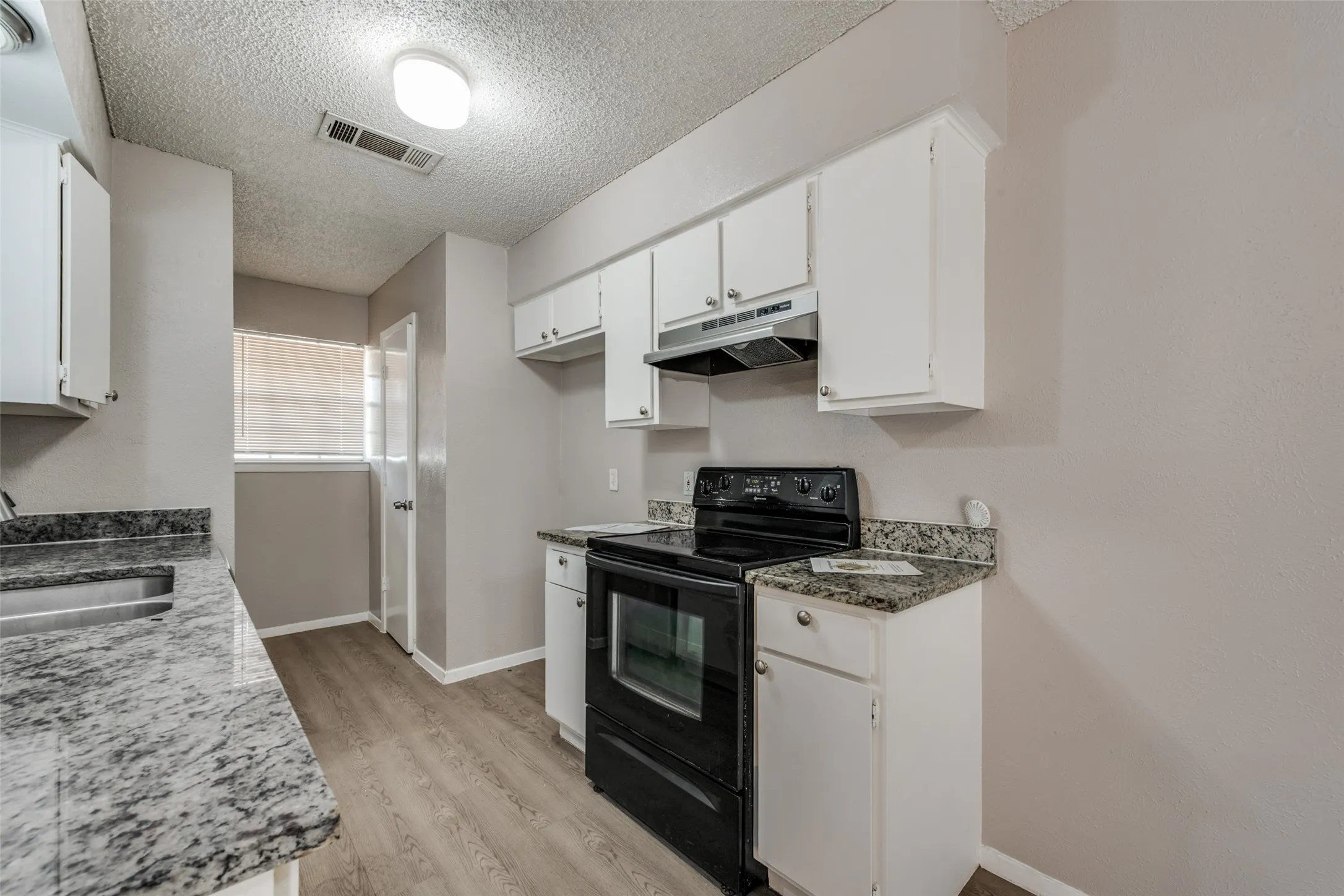 Kitchen featuring white cabinetry, stone-finish countertops, wood-finish flooring, and a black range