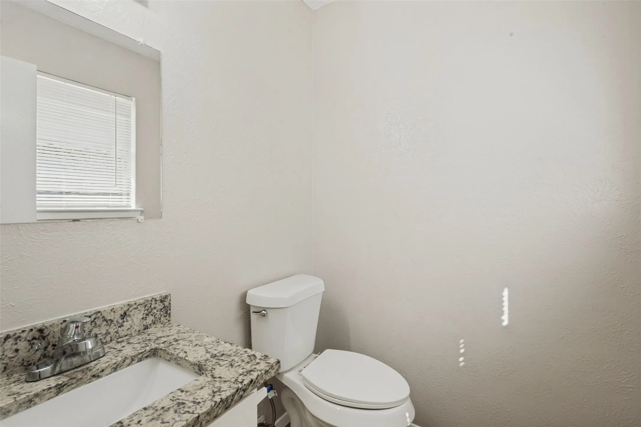 White vanity with a stone-finish countertop, undermount sink, and chrome faucet