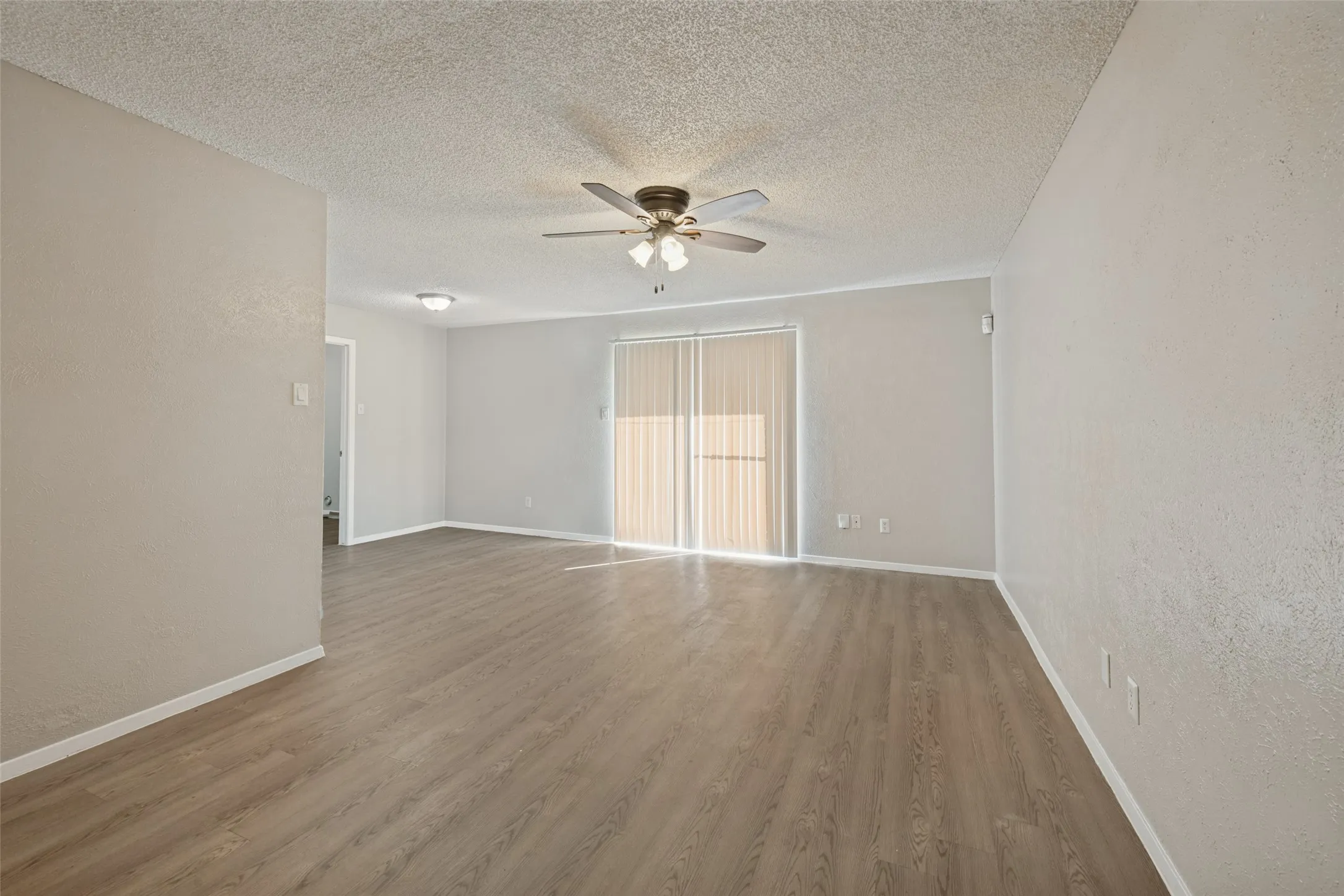 Open living space featuring wood-finish flooring, light-toned walls, and a ceiling fan with integrated lighting