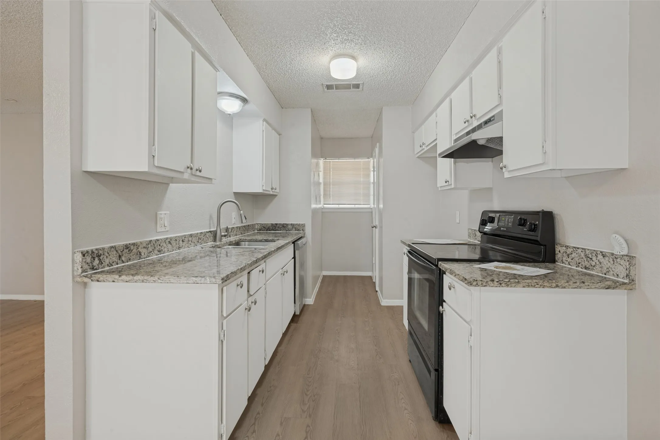 Galley kitchen featuring wood-finish flooring, white cabinetry, granite-style countertops, a stainless steel sink with a high-arc faucet, and an electric range with an overhead microwave