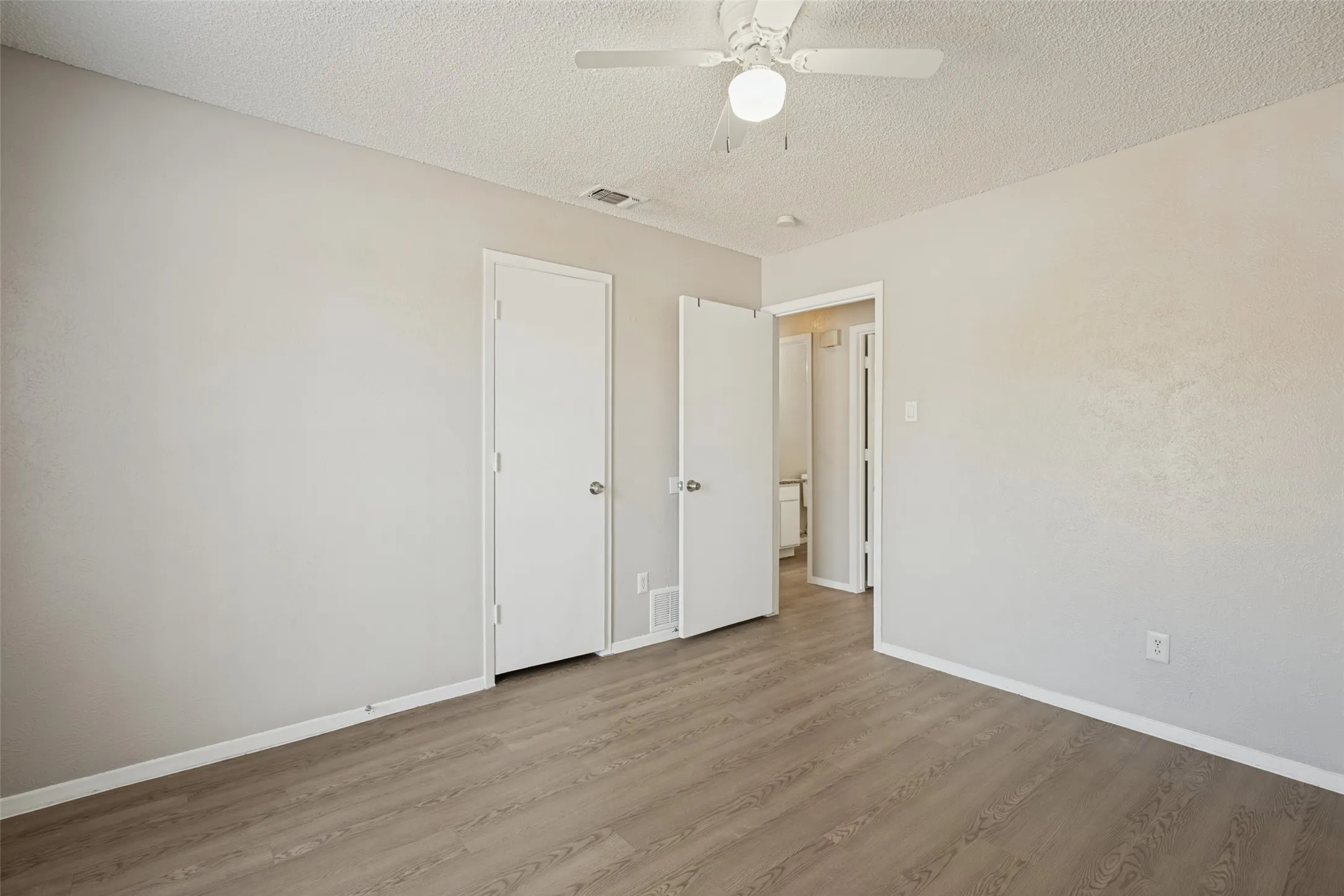 Wood-finish flooring, neutral wall tones, white interior doors, and a ceiling fan with integrated lighting