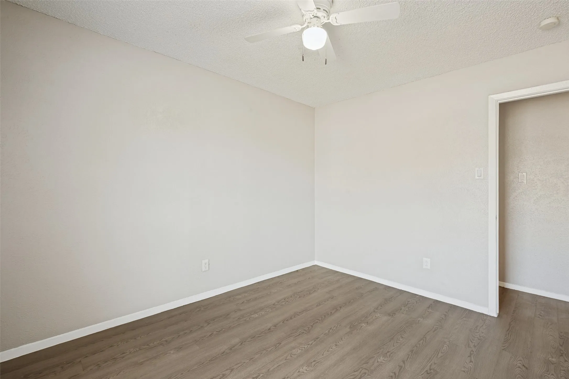 Wood-finish flooring, neutral wall tones, and a ceiling fan with integrated lighting
