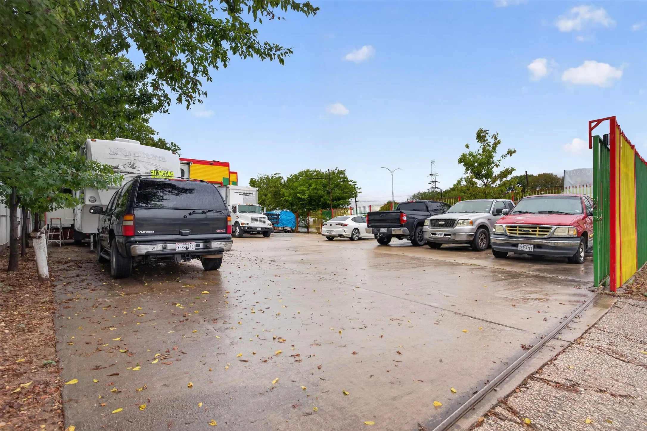 Paved parking area featuring a colorful gate and surrounding trees