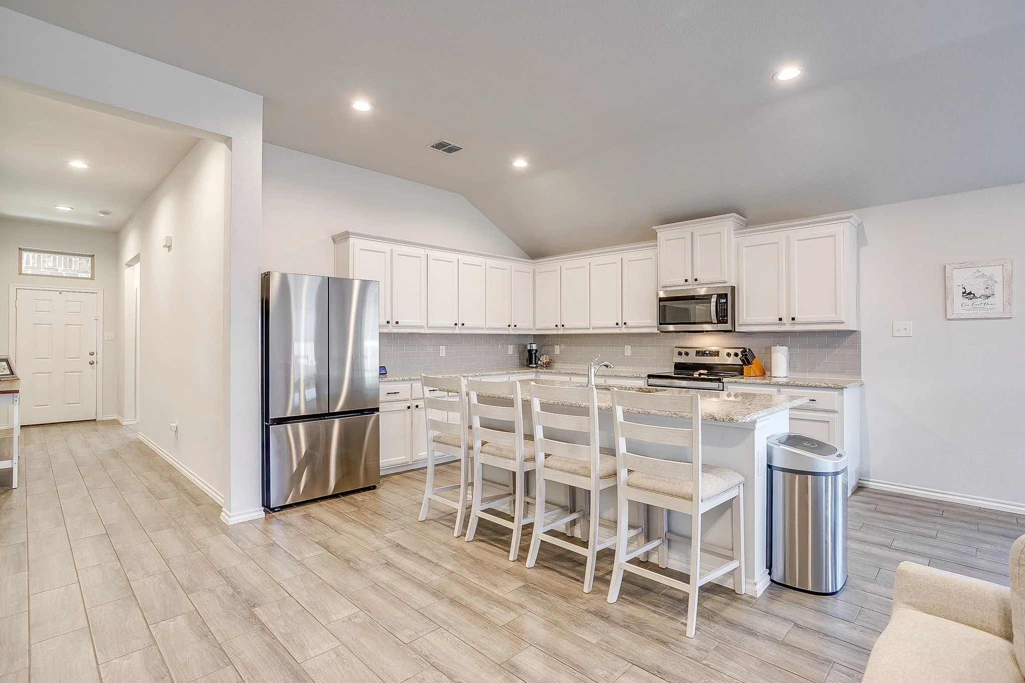 Kitchen featuring white cabinetry, stainless steel appliances, a center island with seating, and wood-finish flooring