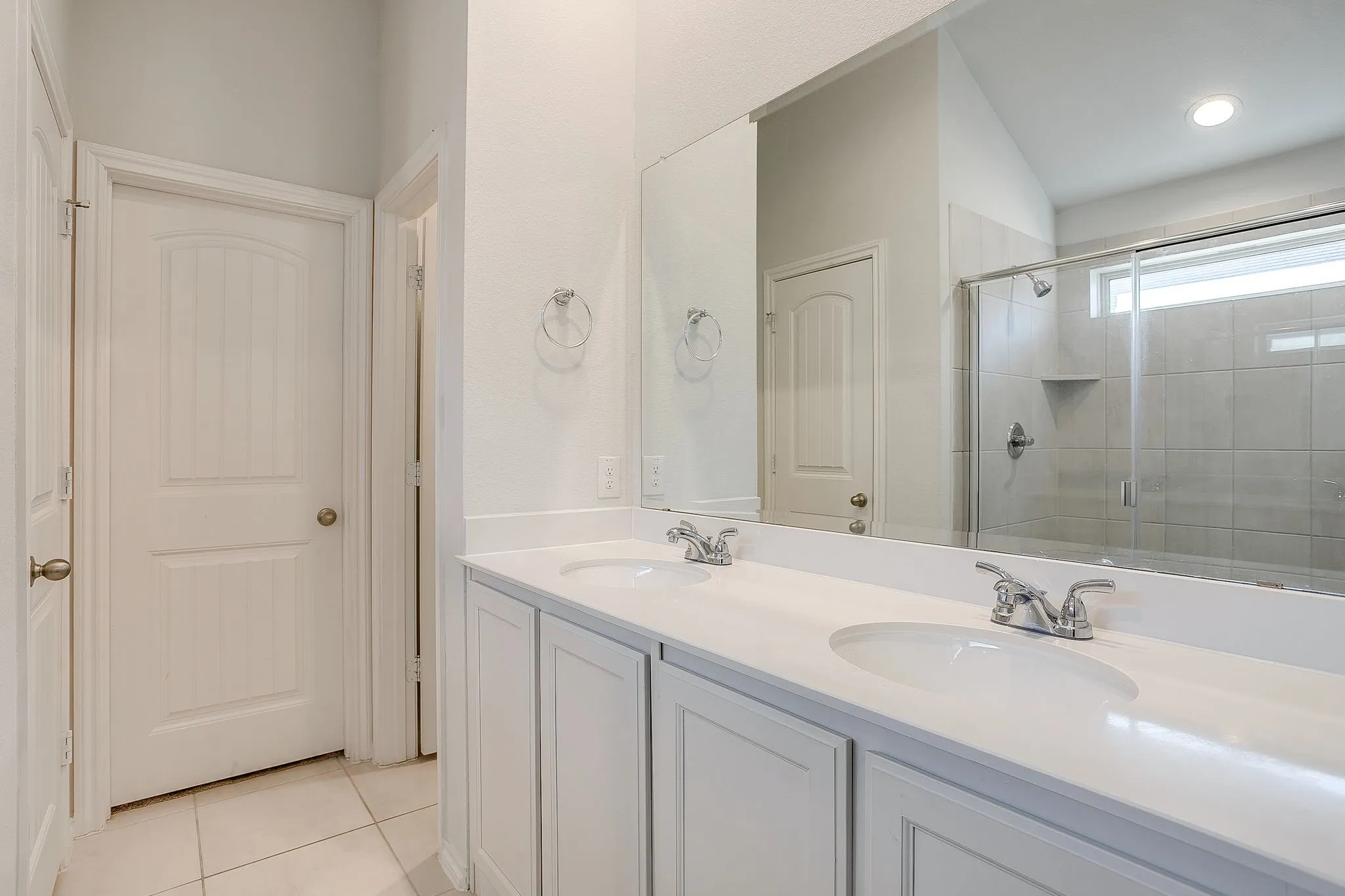 Dual vanity with white cabinetry and chrome fixtures, large mirror, tiled flooring, and a glass-enclosed shower with tiled walls