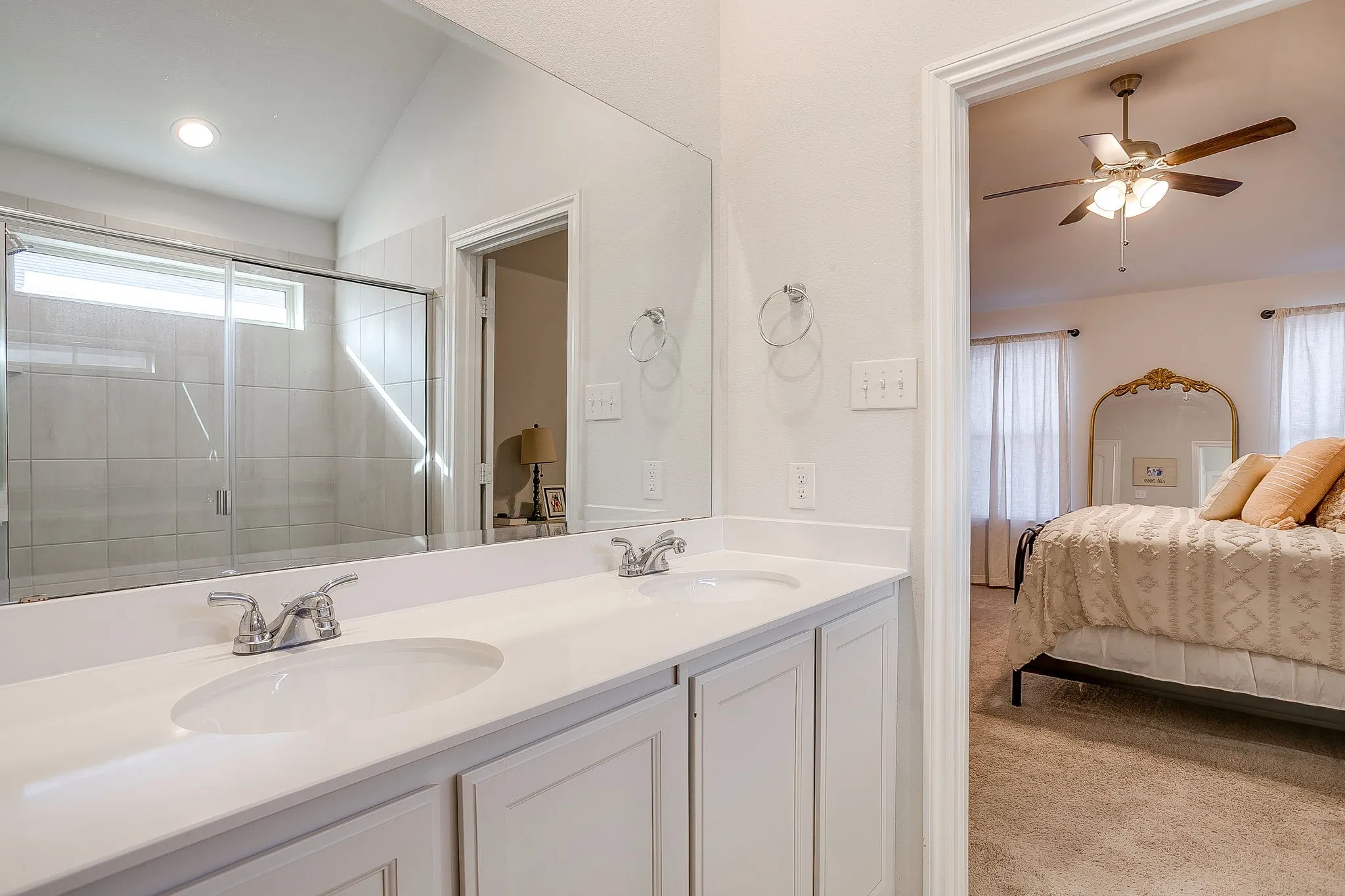 Double vanity with integrated sinks, framed mirror, and enclosed shower with a transom window