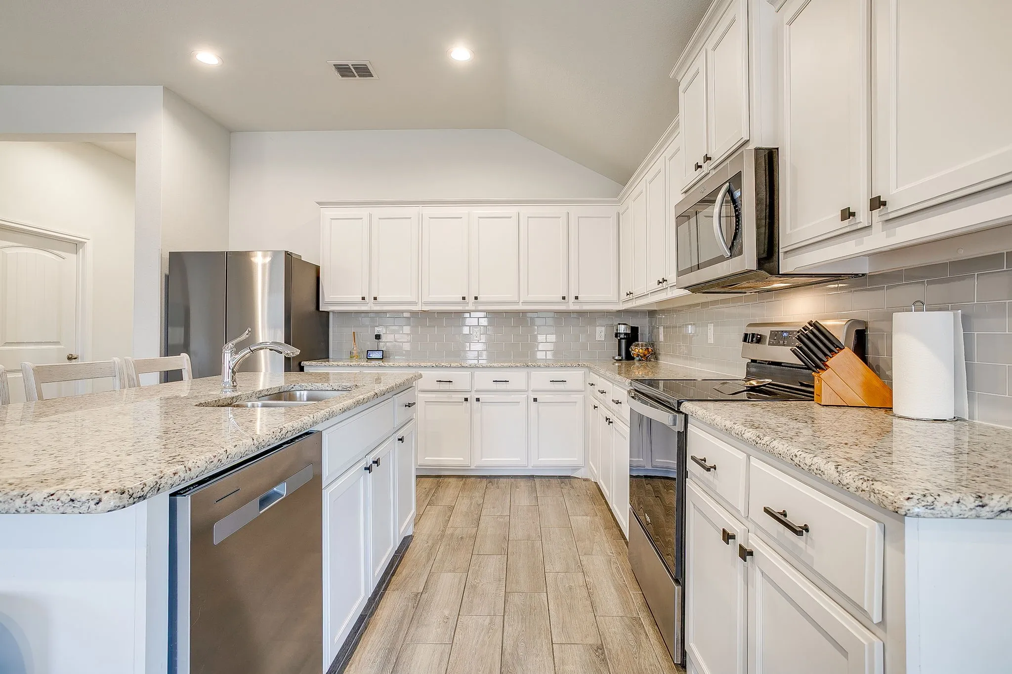 White cabinetry with dark hardware, stone-finish countertops, stainless steel appliances, tile backsplash, and wood-finish flooring