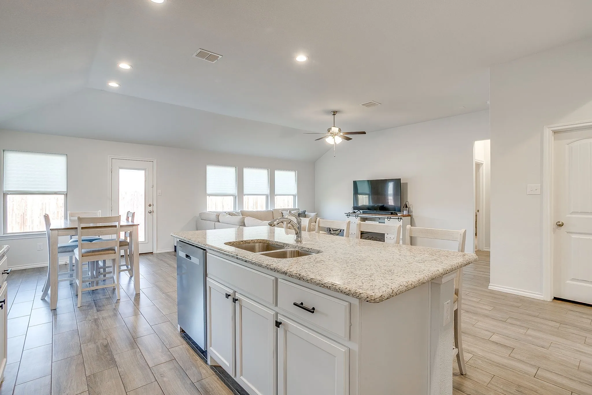 Open-concept living space with vaulted ceilings, wood-finish flooring, a kitchen island with a double basin sink, and recessed lighting