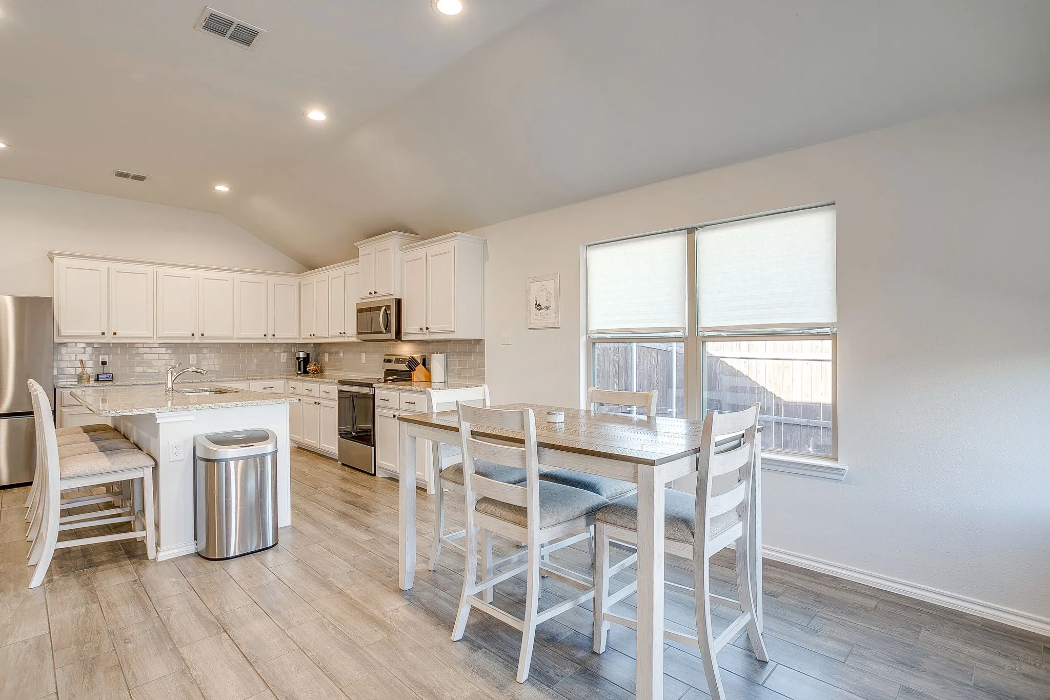 Vaulted ceiling with recessed lighting, white cabinetry, light-toned wood-finish flooring, stainless steel appliances, and a kitchen island with seating