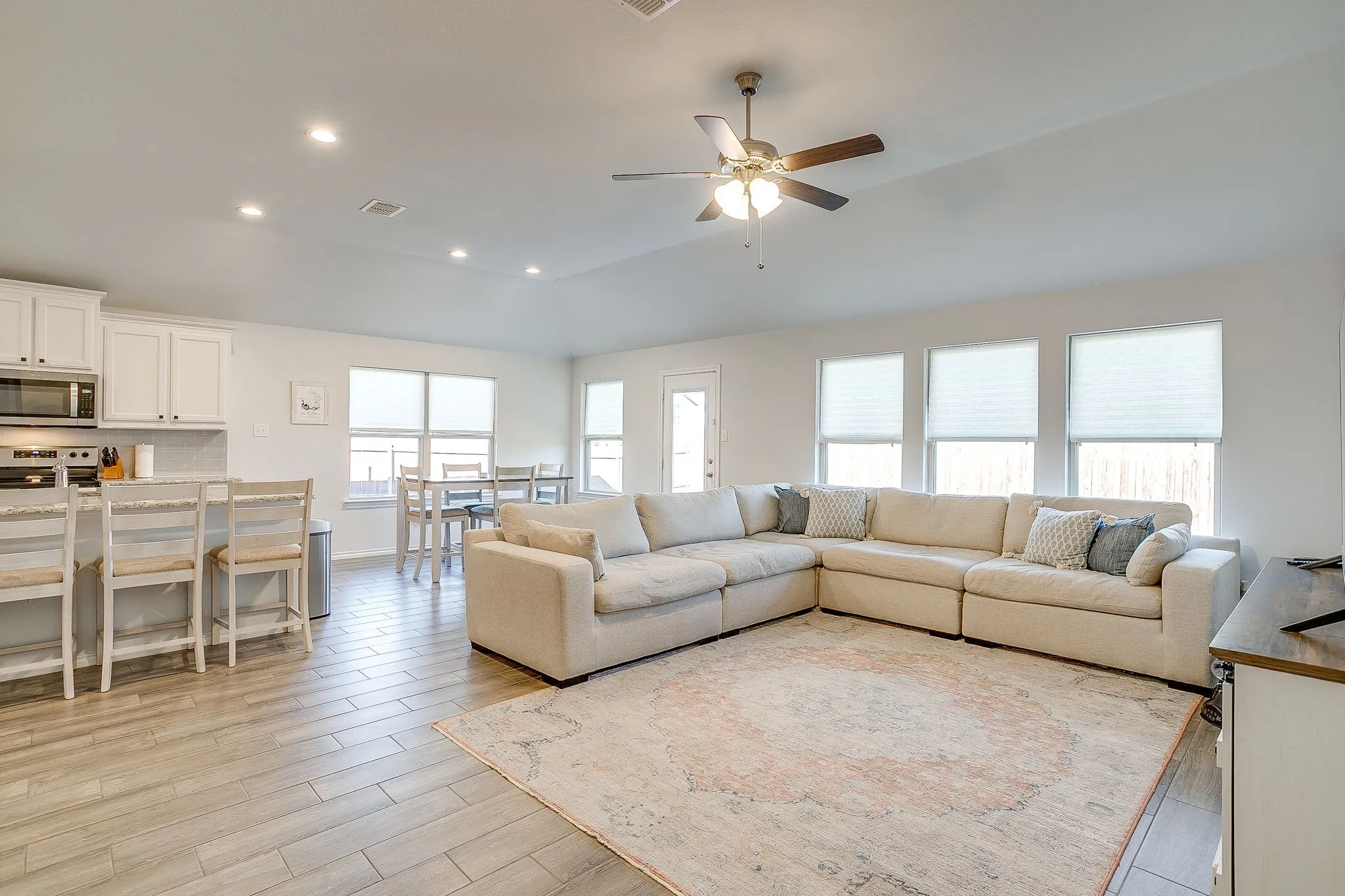 Open-concept living area with wood-finish flooring, recessed lighting, white cabinetry, and multiple windows