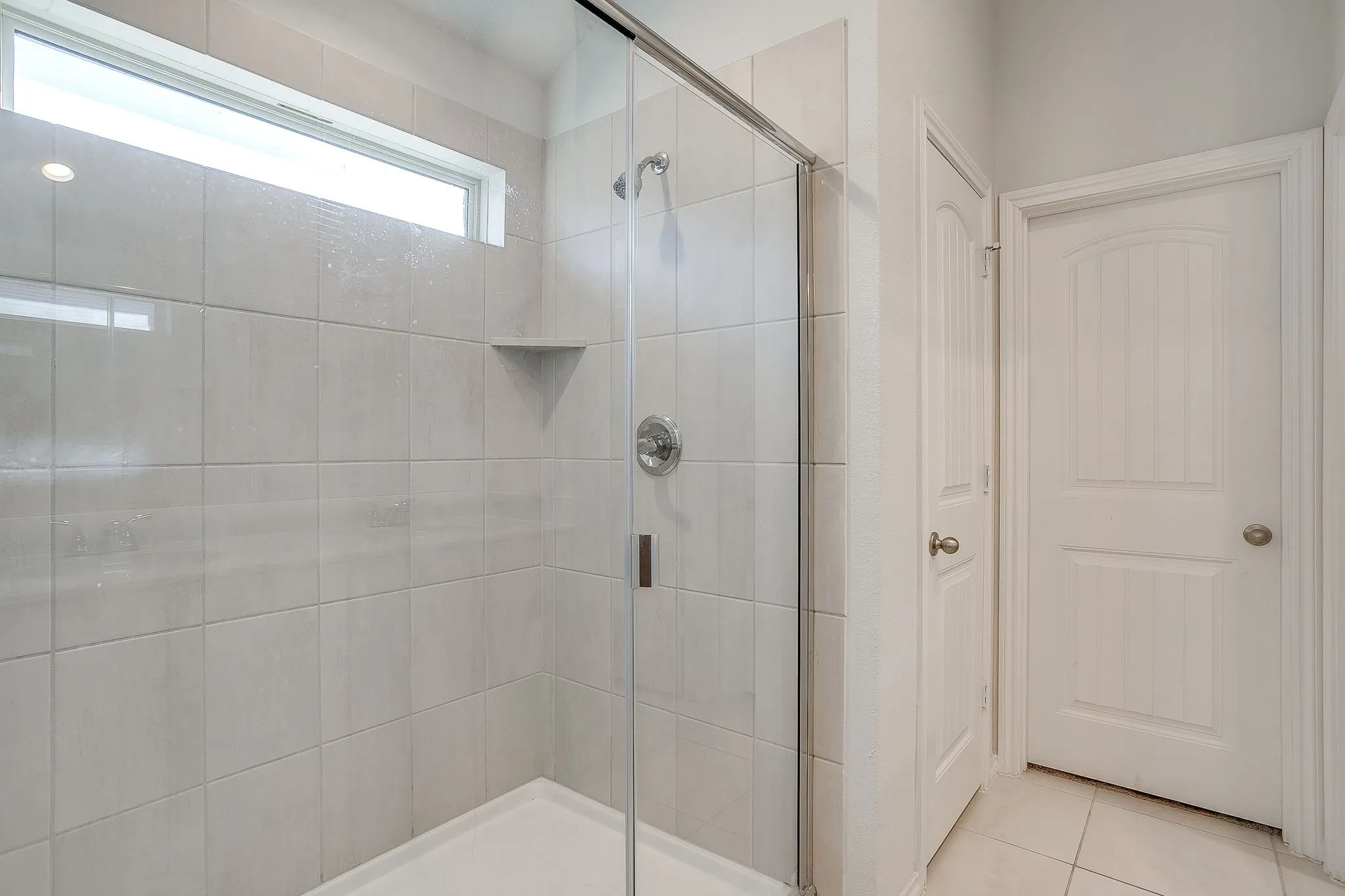 Tiled shower with glass enclosure, chrome fixtures, and built-in corner shelf