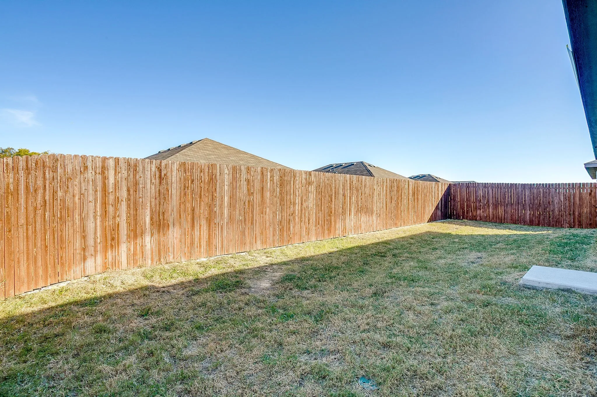 Expansive backyard with a wooden privacy fence, natural grass, and a concrete pad