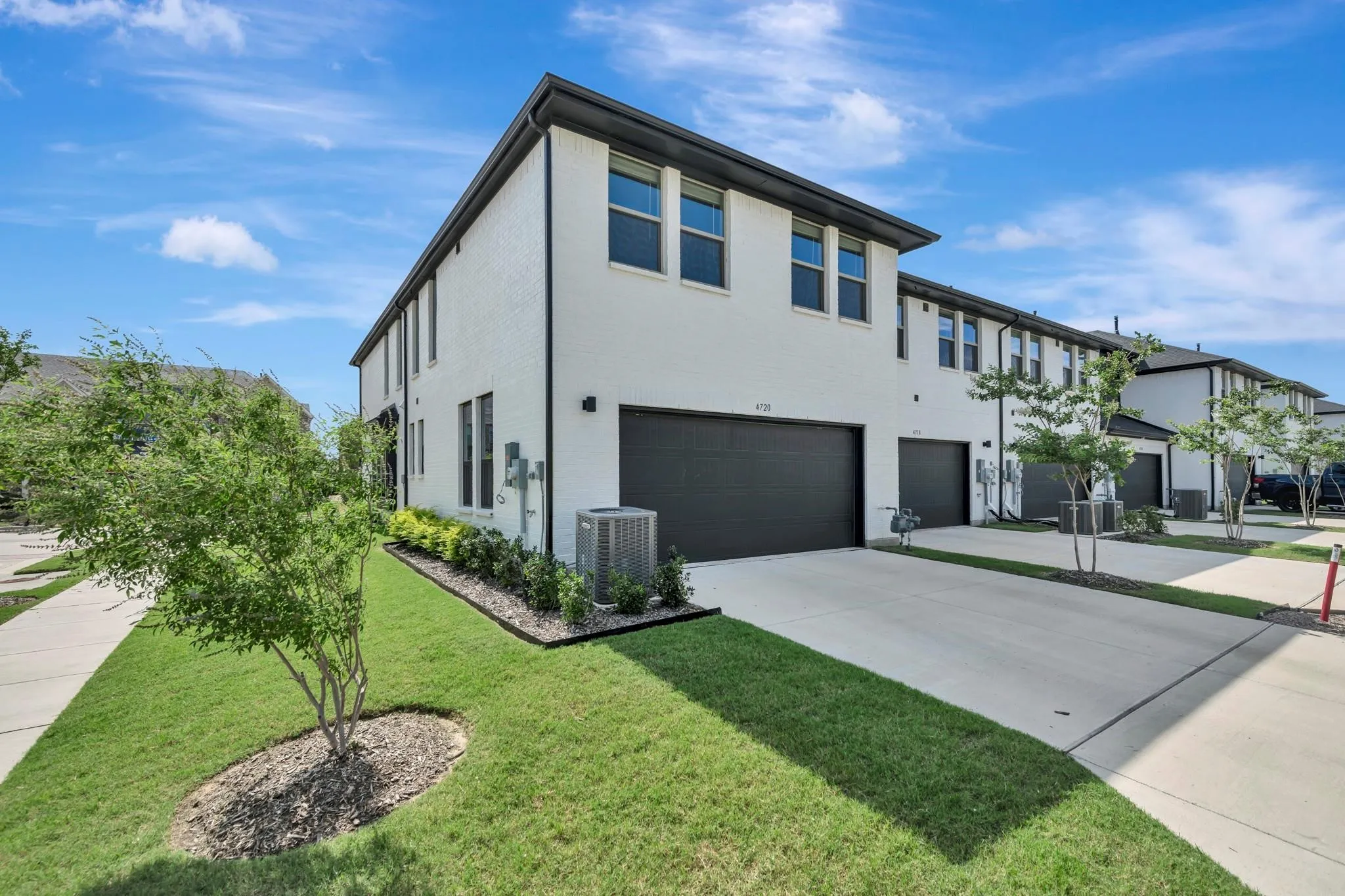 White brick exterior, black trim windows, two-car garage, concrete driveway, and manicured landscaping
