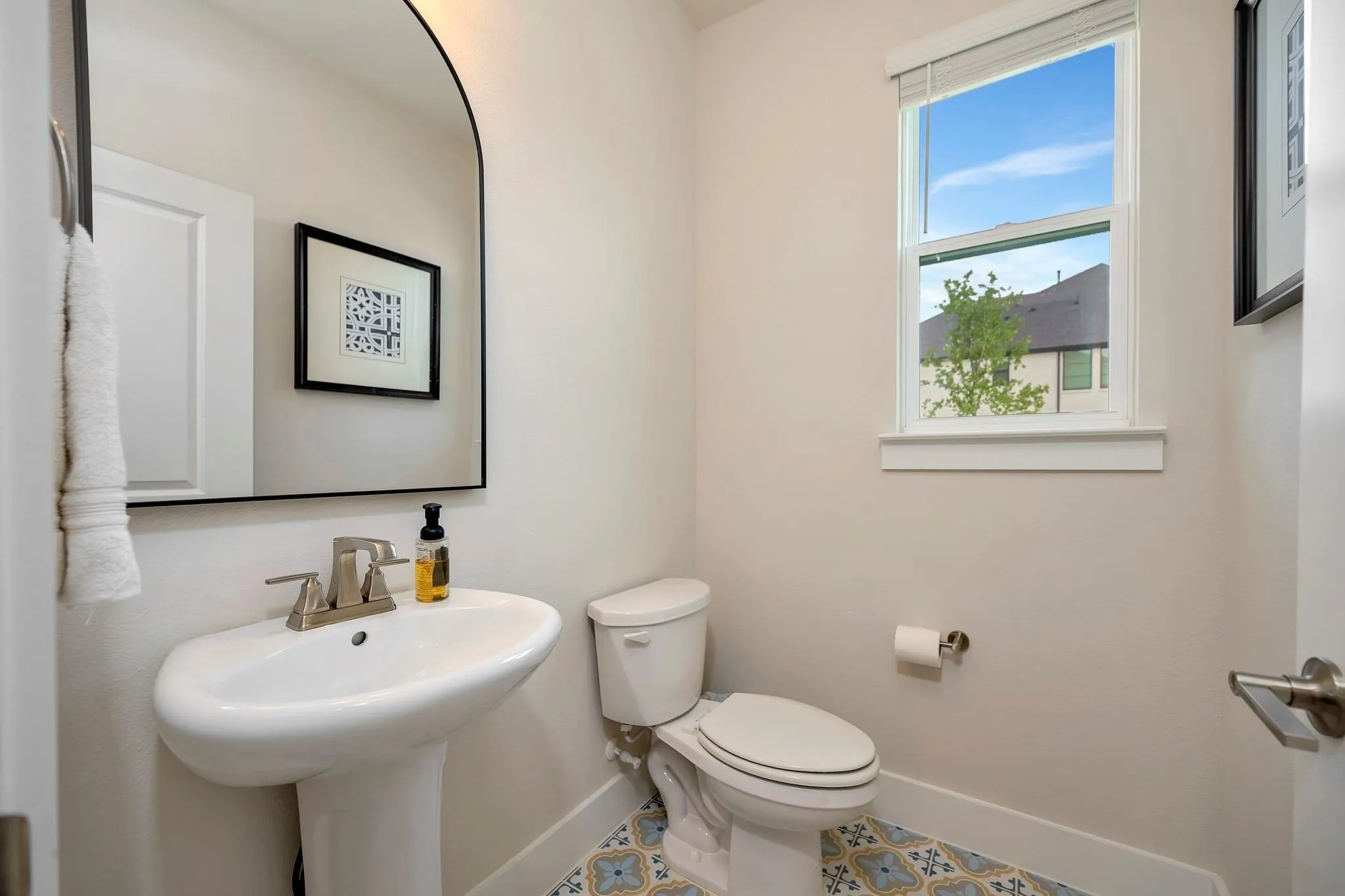Pedestal sink with brushed nickel faucet, arched mirror, single window, and patterned floor tile