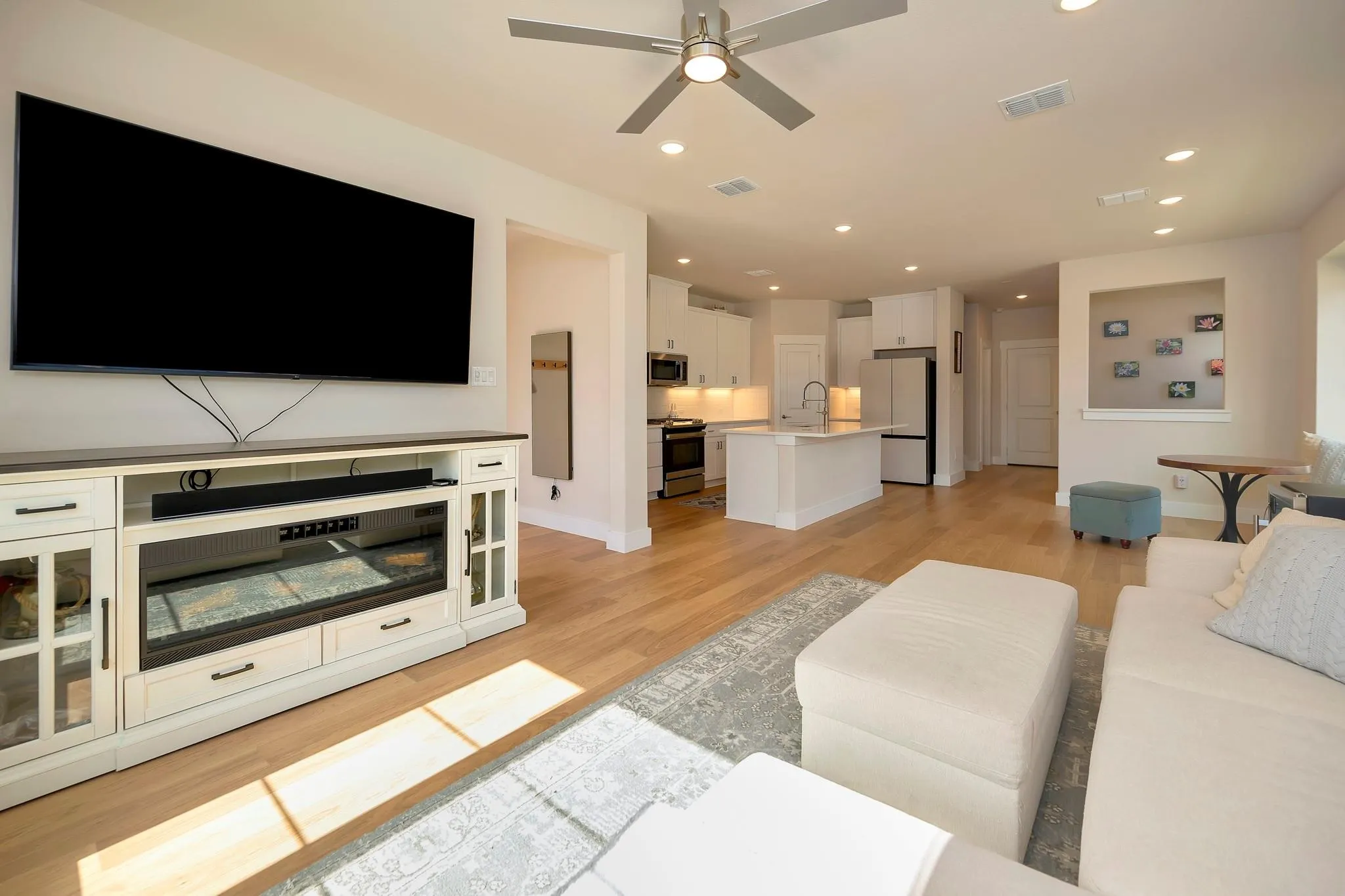 Open-concept living area featuring light wood-finish flooring, recessed lighting, a modern ceiling fan, and a white kitchen with a central island