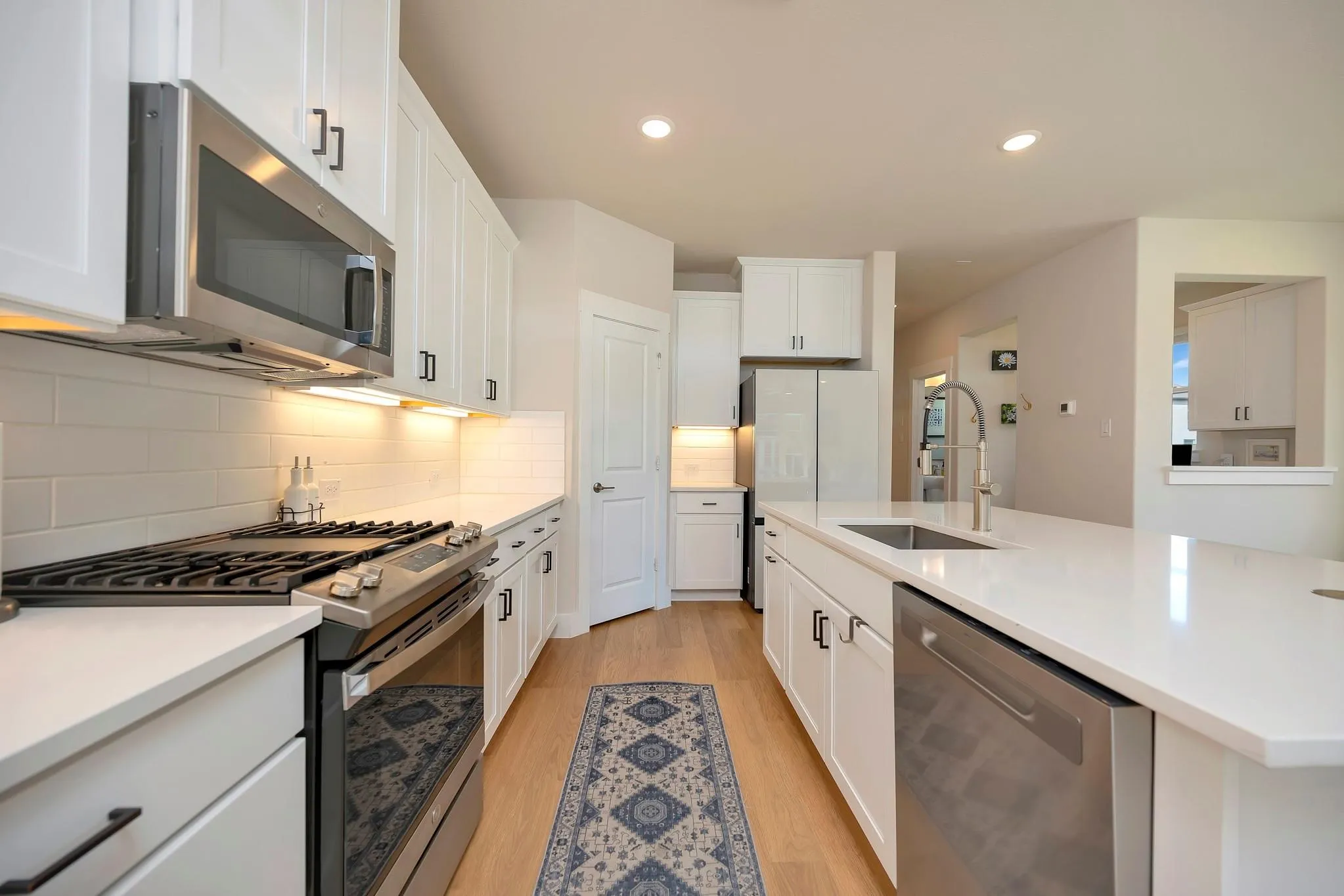 Kitchen featuring white cabinetry with dark hardware, stainless steel appliances, solid surface countertops, and wood-finish flooring