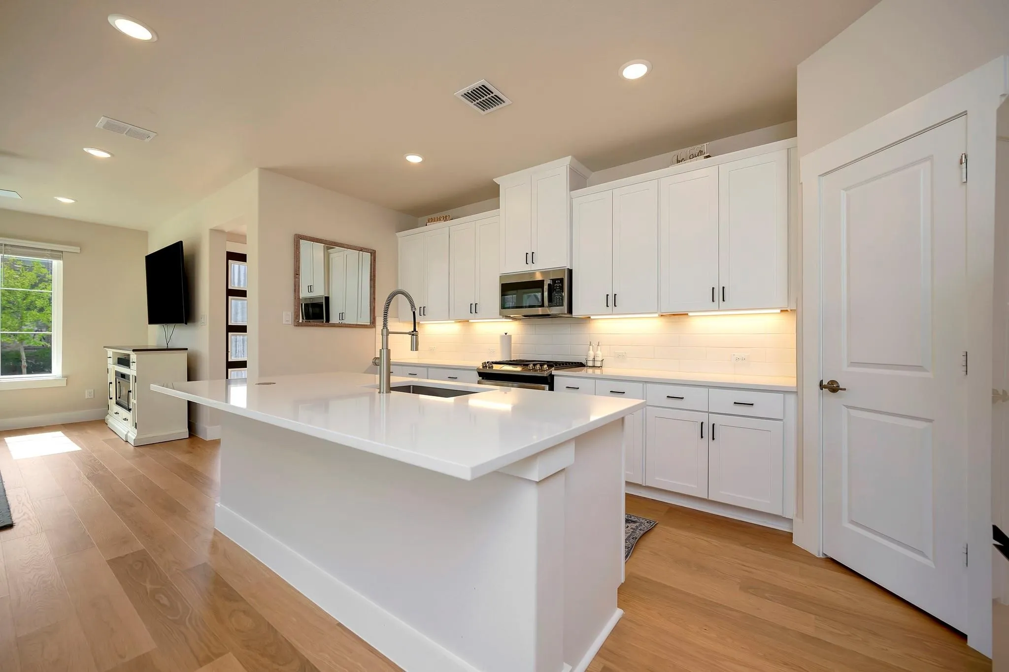 Kitchen featuring an expansive island with a waterfall countertop, integrated sink with a gooseneck faucet, white cabinetry with under-cabinet lighting, a subway tile backsplash, and wood-finish flooring