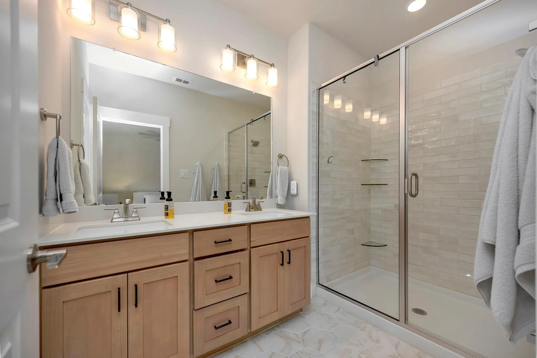 Dual vanity with light wood-finish cabinetry, white countertops, and chrome fixtures