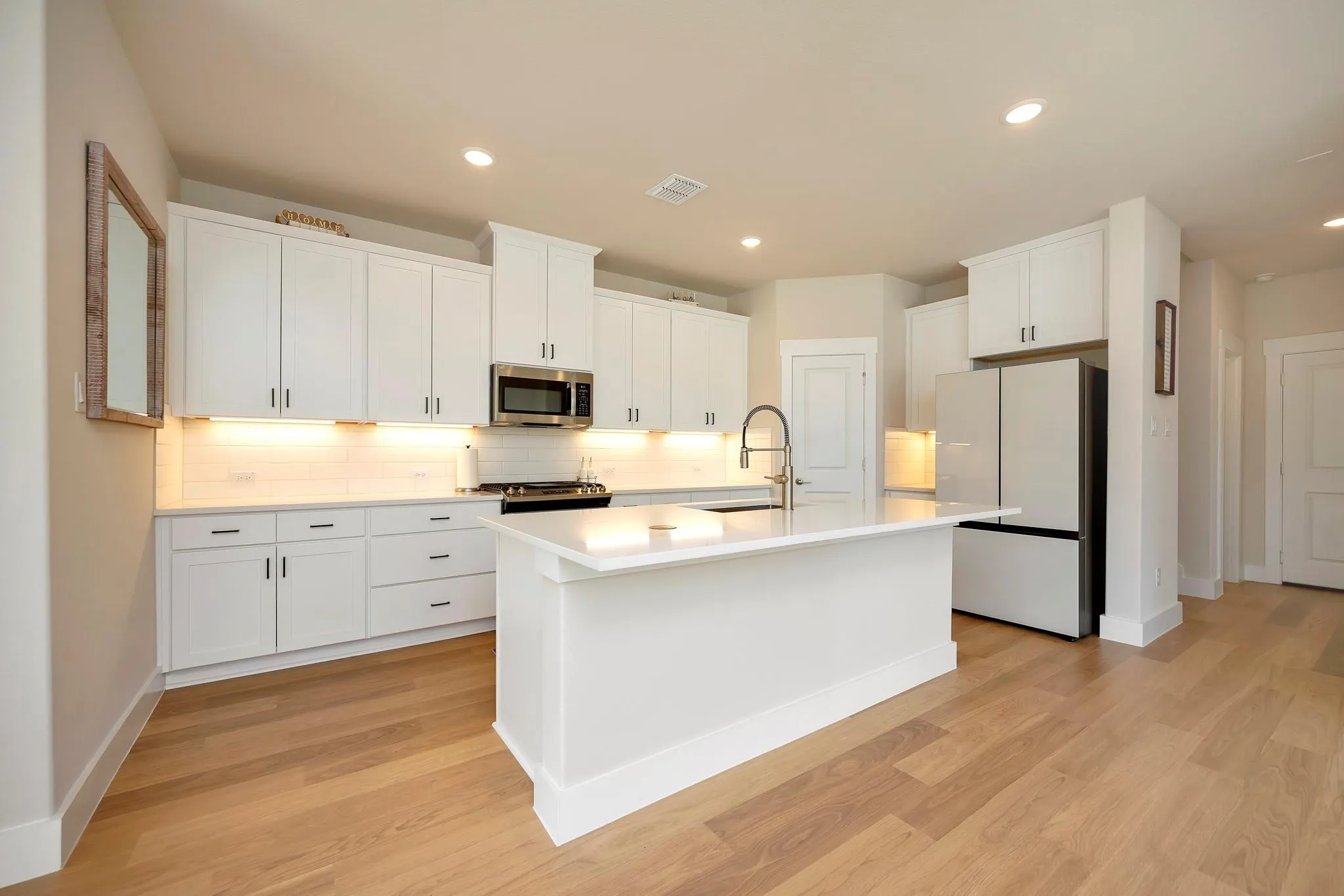 Modern kitchen with wood-finish flooring, white cabinetry, integrated stainless steel appliances, a center island with a sink, and recessed lighting