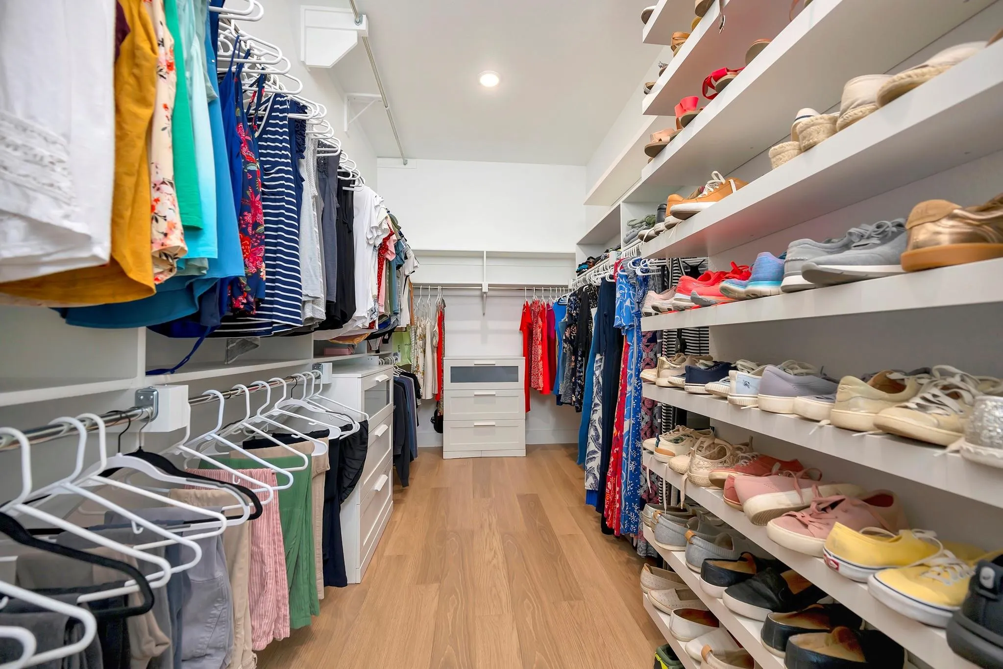 Custom closet system with extensive shelving, multiple hanging rods, built-in drawer storage, recessed lighting, and wood-finish flooring