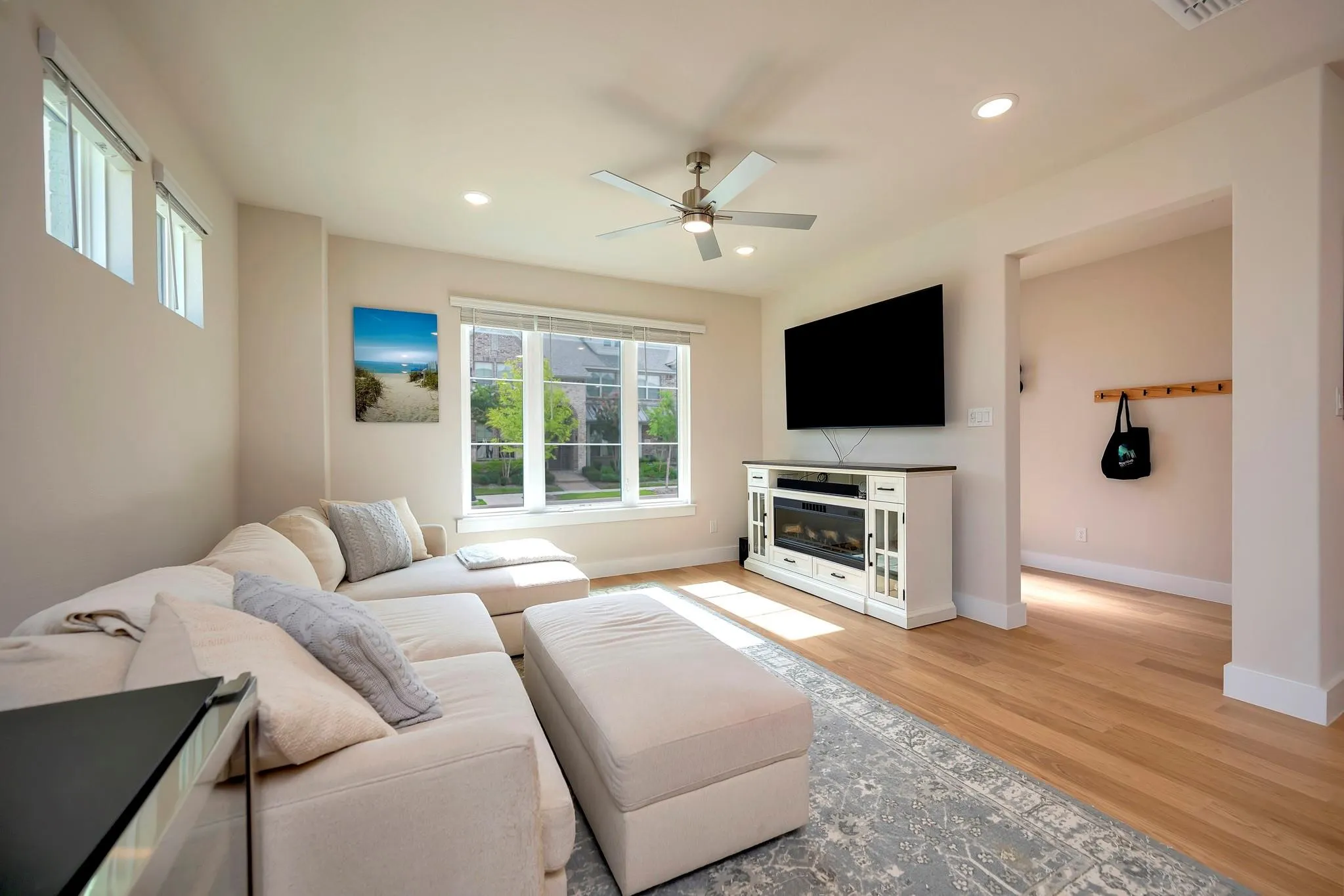 Hardwood flooring, recessed lighting, ceiling fan, multiple windows, and a built-in media console with an electric fireplace