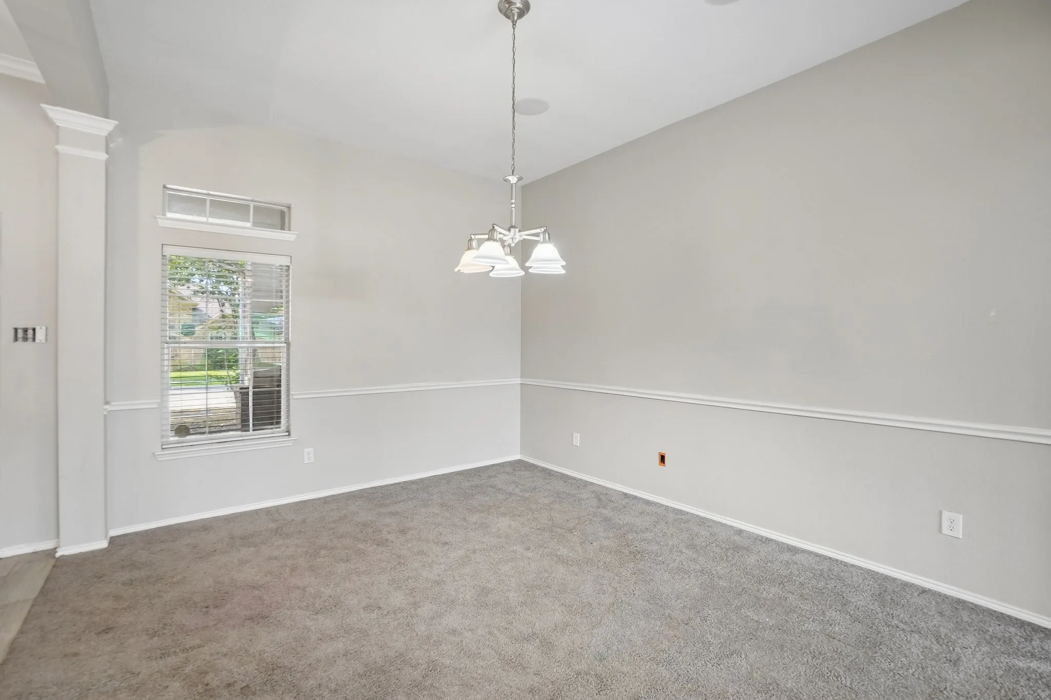 Vaulted ceiling with an attached chandelier, crown molding, and a window with blinds