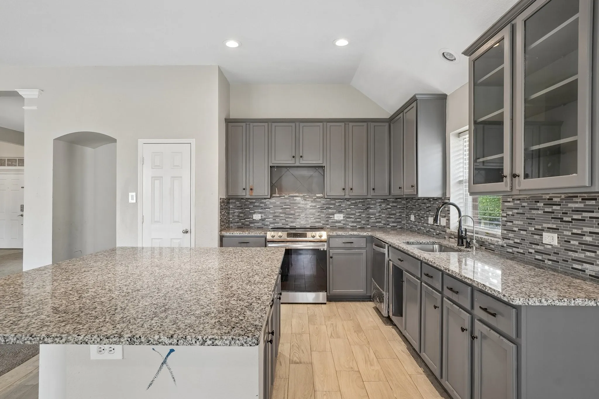 Kitchen featuring gray cabinetry, granite countertops, a mosaic tile backsplash, wood-finish flooring, and stainless steel appliances