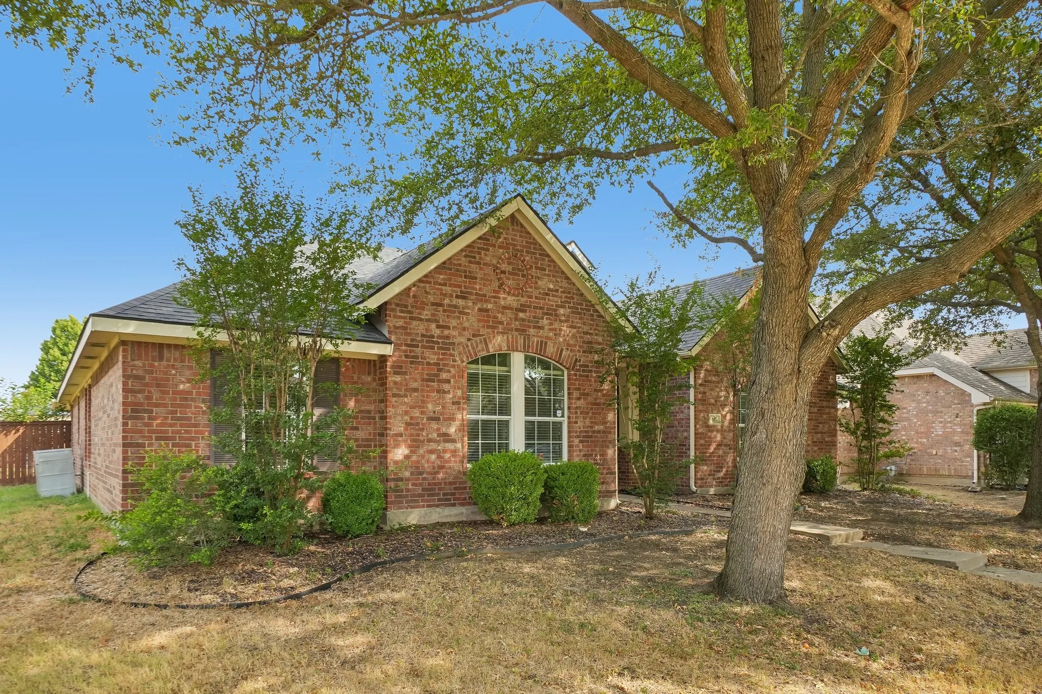 Brick exterior with an arched window, dark shingle roof, and established trees