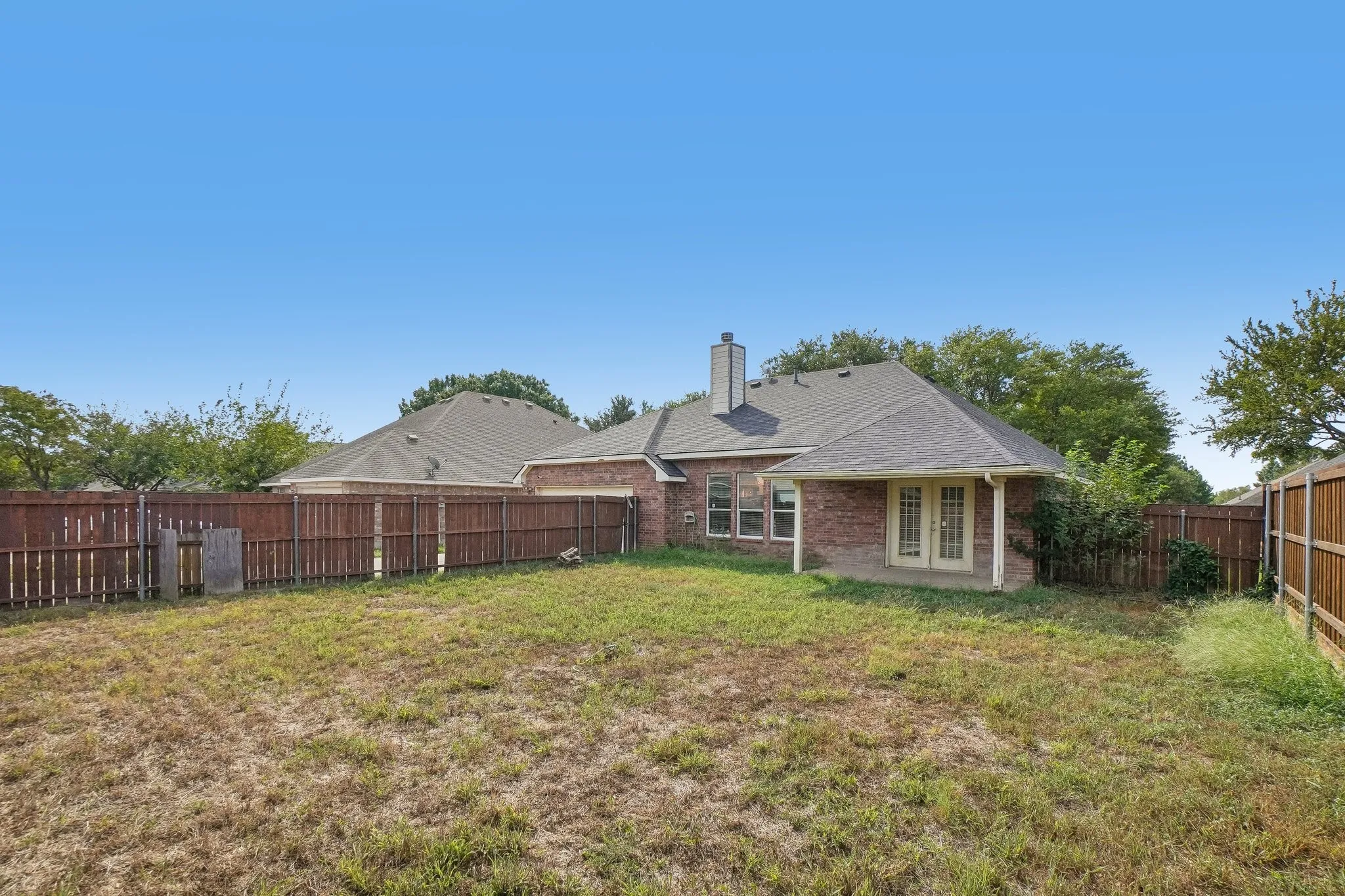 Expansive backyard with a full privacy fence and a covered concrete patio