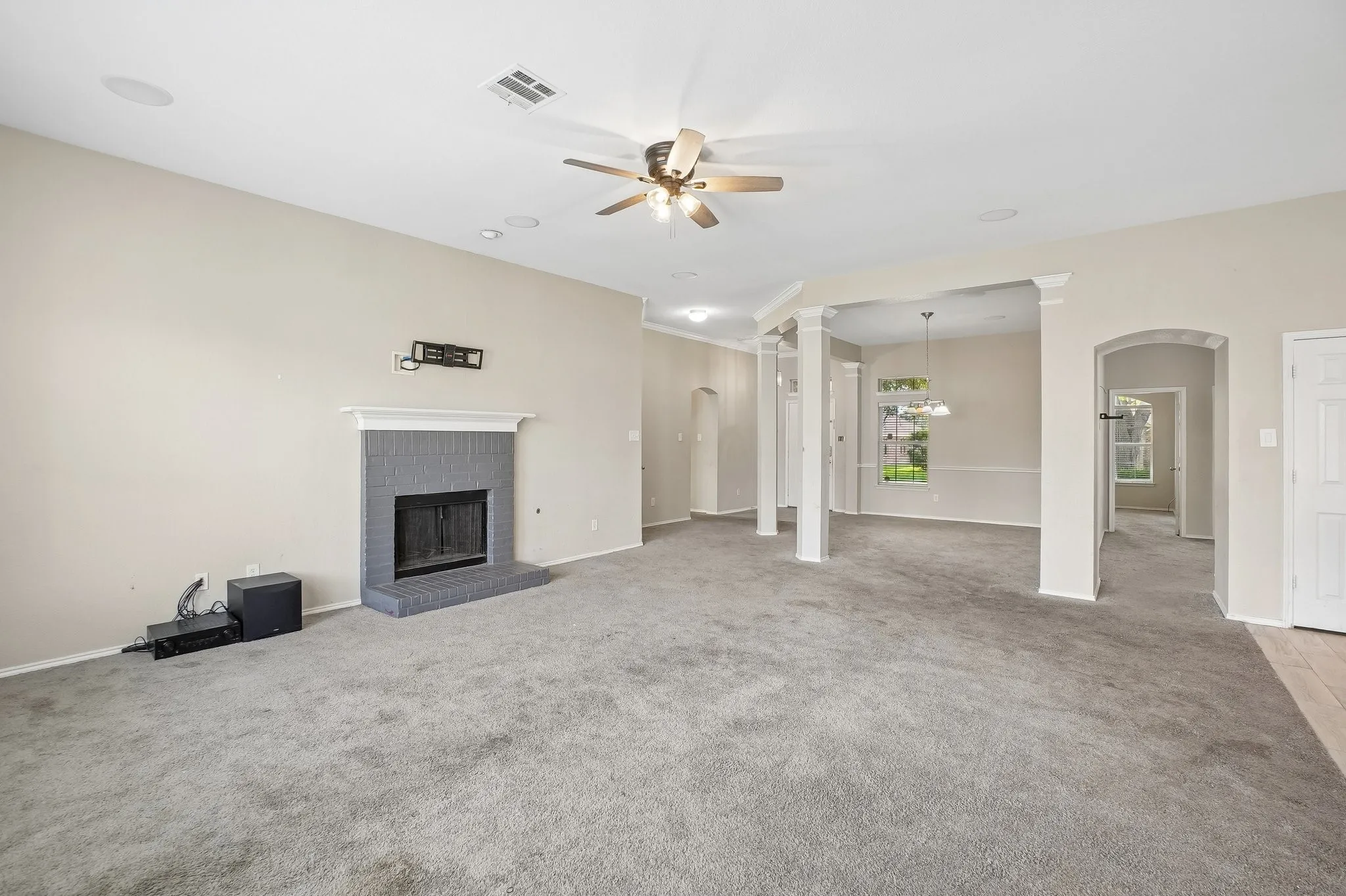 Spacious living area featuring a fireplace with a gray brick surround and white mantel, ceiling fan, recessed lighting, and architectural columns