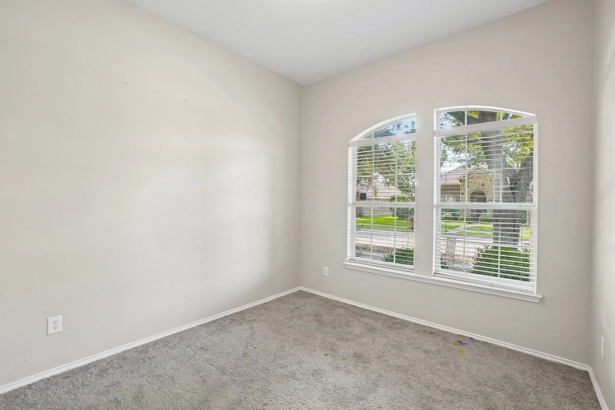 Arched windows with blinds, light gray wall paint, and gray carpeted flooring