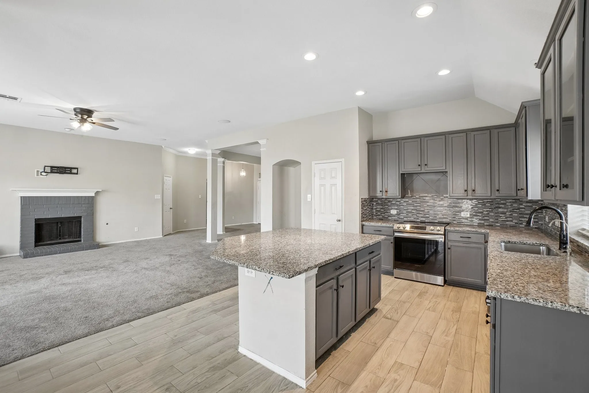 Kitchen featuring gray cabinetry, granite countertops, tile backsplash, and stainless steel range