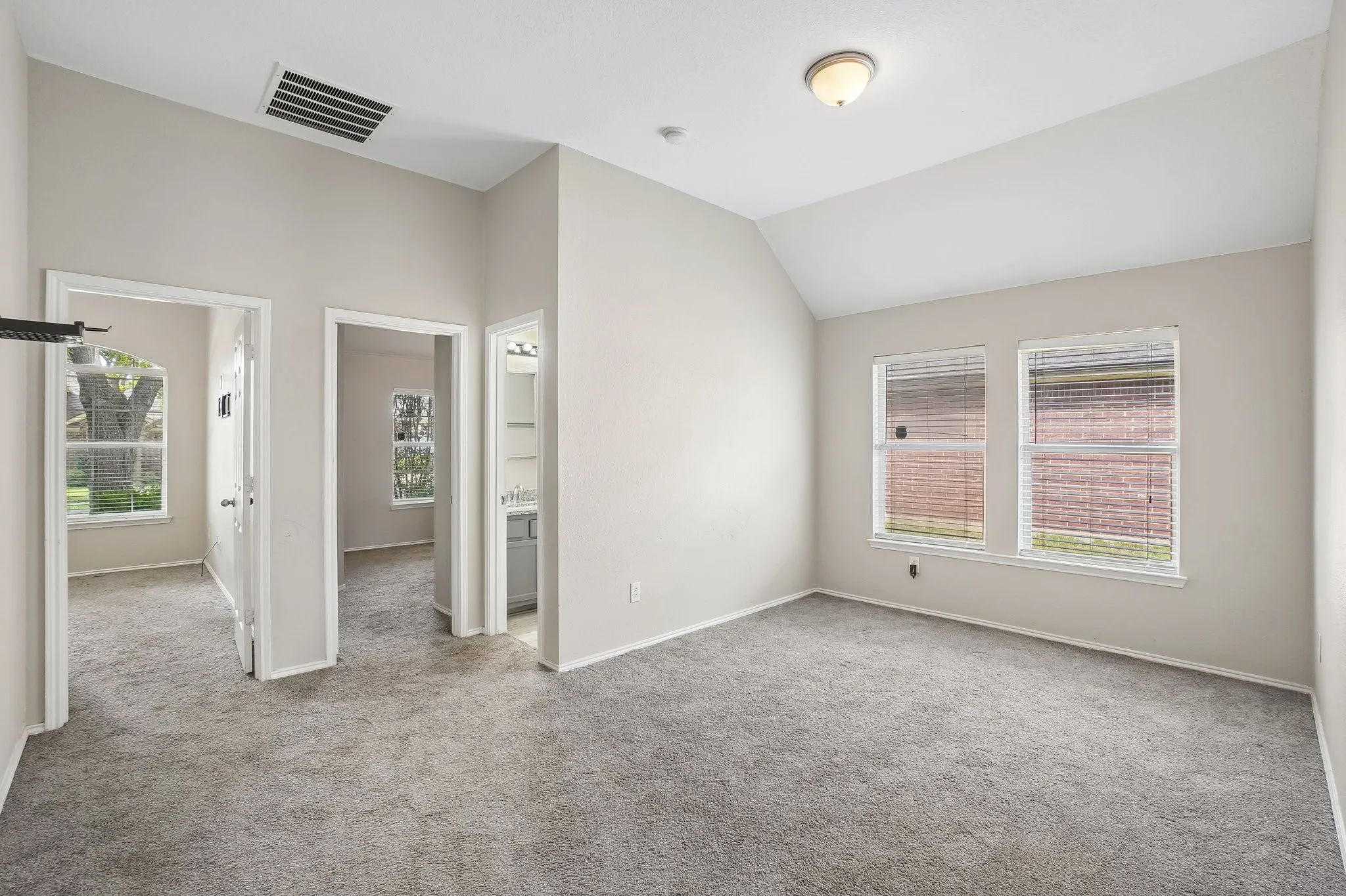 Vaulted ceiling with an overhead light fixture, light gray carpeting, two windows with blinds, and white trim throughout