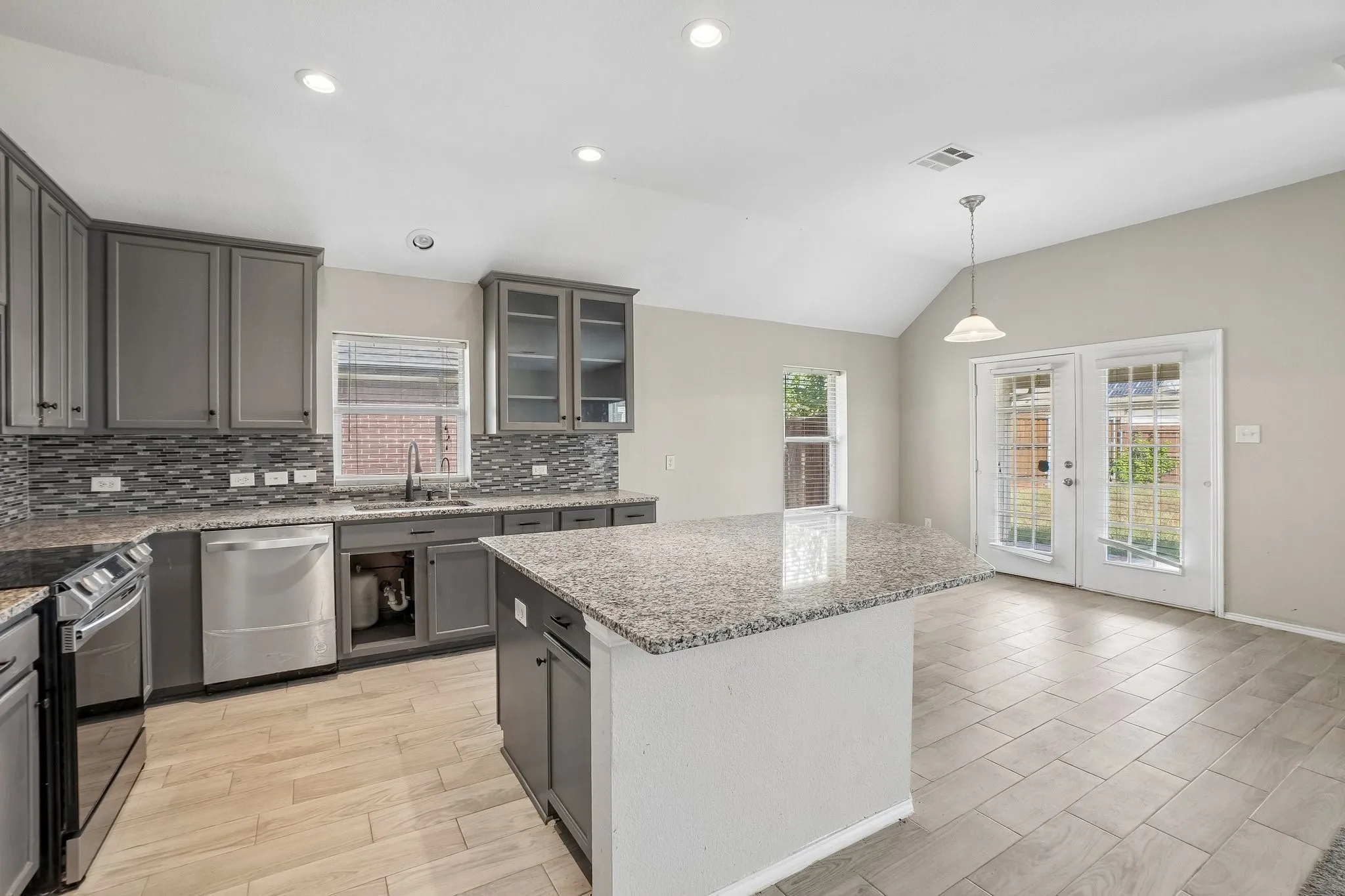 Kitchen featuring an island, grey cabinetry, stainless steel appliances, and granite countertops