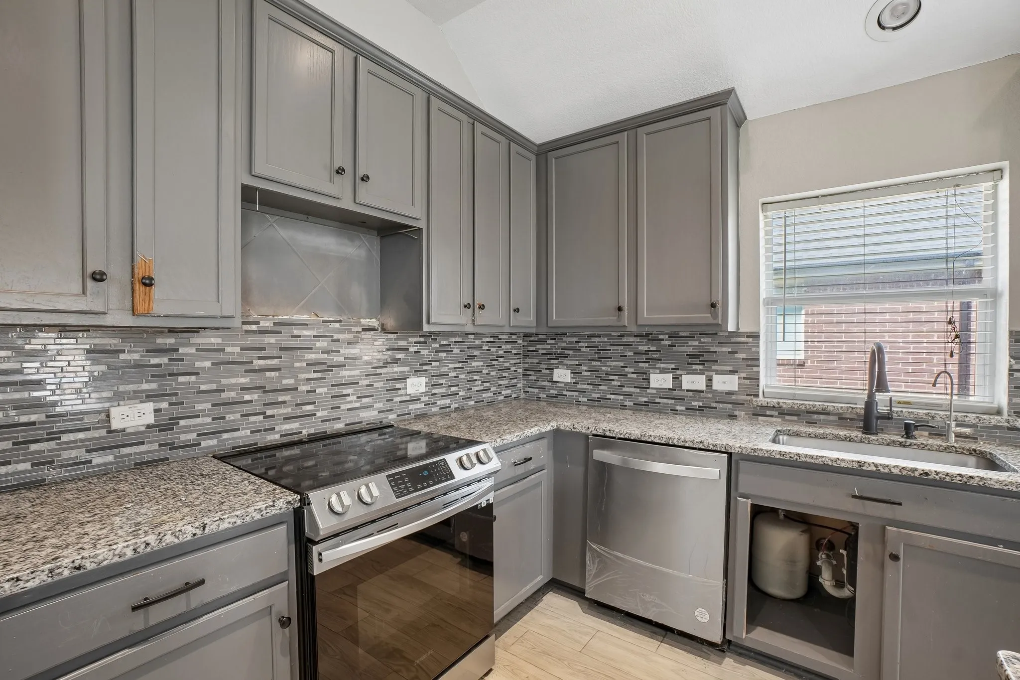 Gray cabinetry, mosaic tile backsplash, stainless steel appliances, granite countertops, and recessed lighting