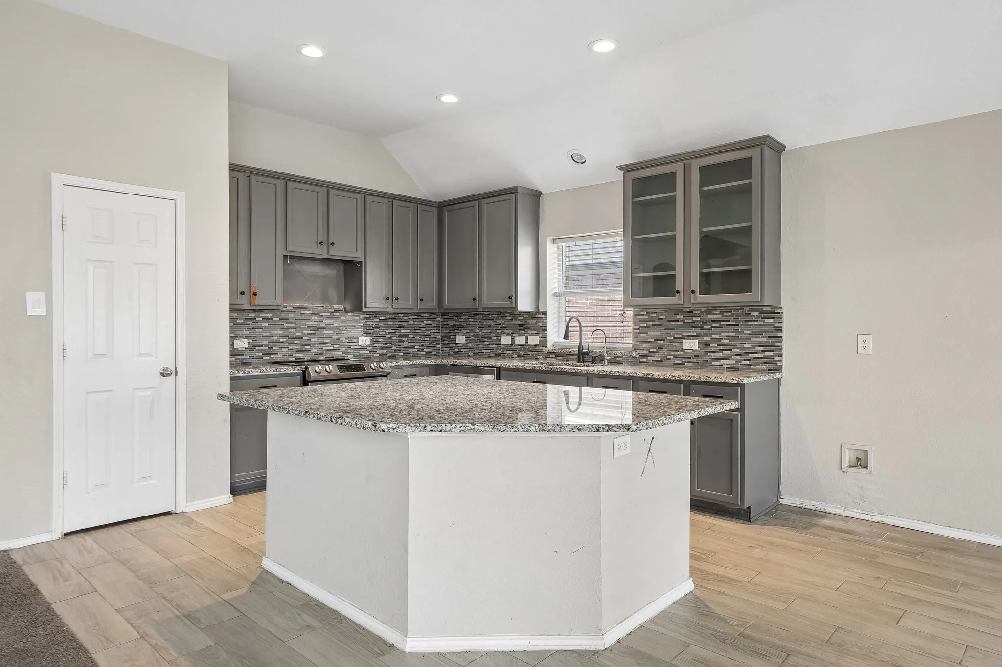 Kitchen featuring grey cabinetry, a multi-tone tile backsplash, and a center island with a light-toned countertop