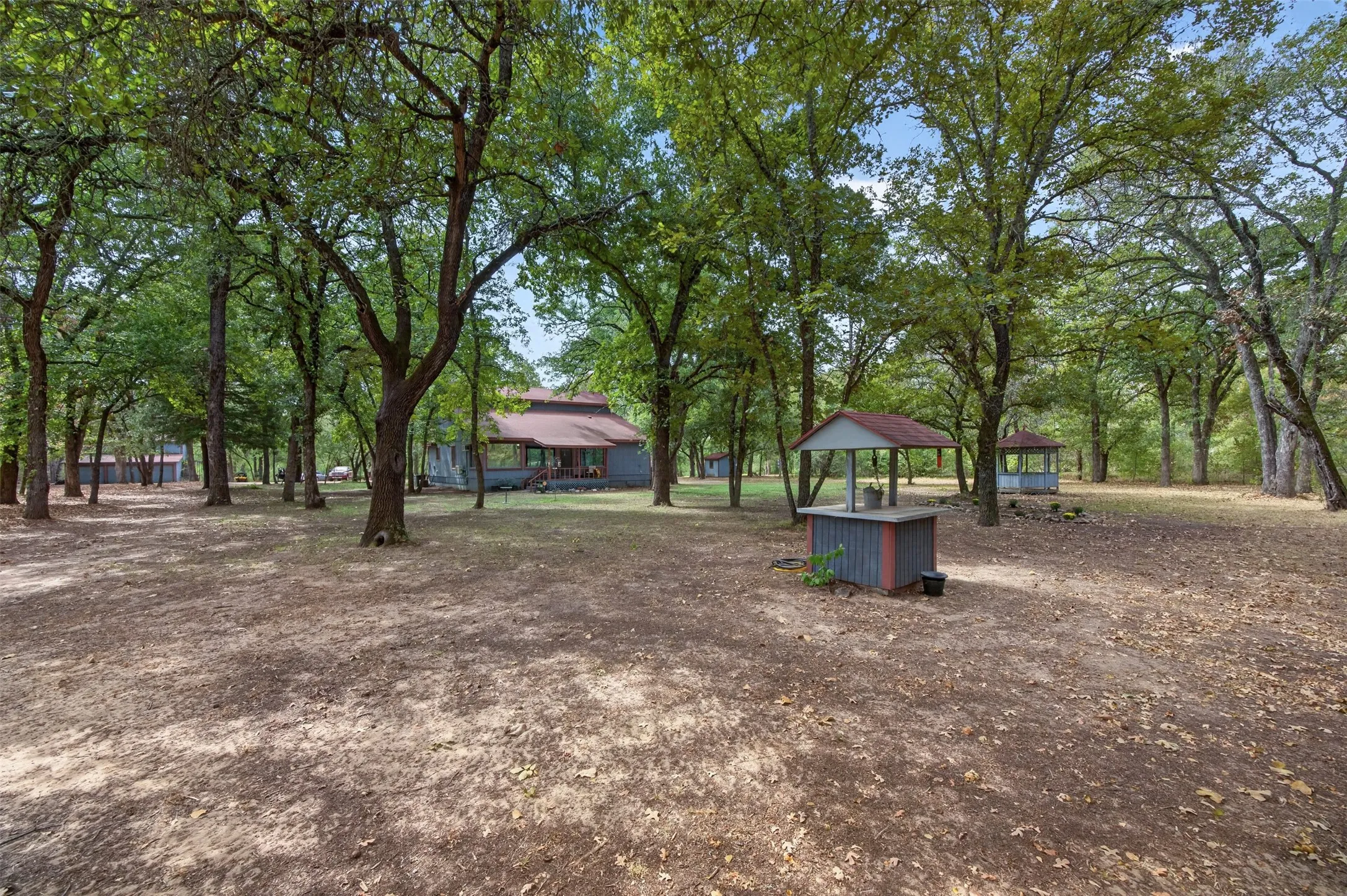 Extensive tree coverage, multiple outbuildings, well structure, and a main residence with a covered porch