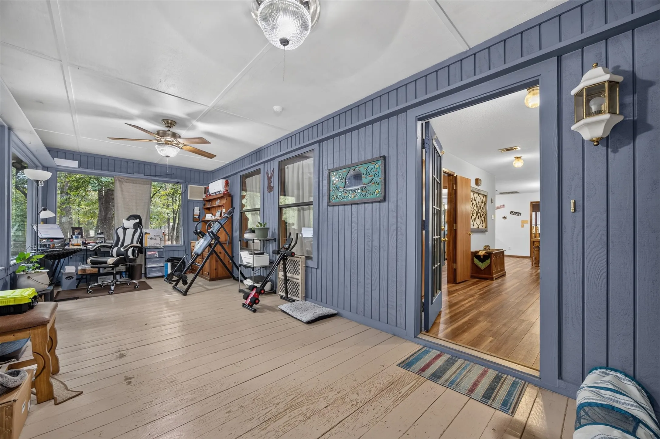 Enclosed porch with wood-finish flooring, blue vertical plank paneling, and multiple windows