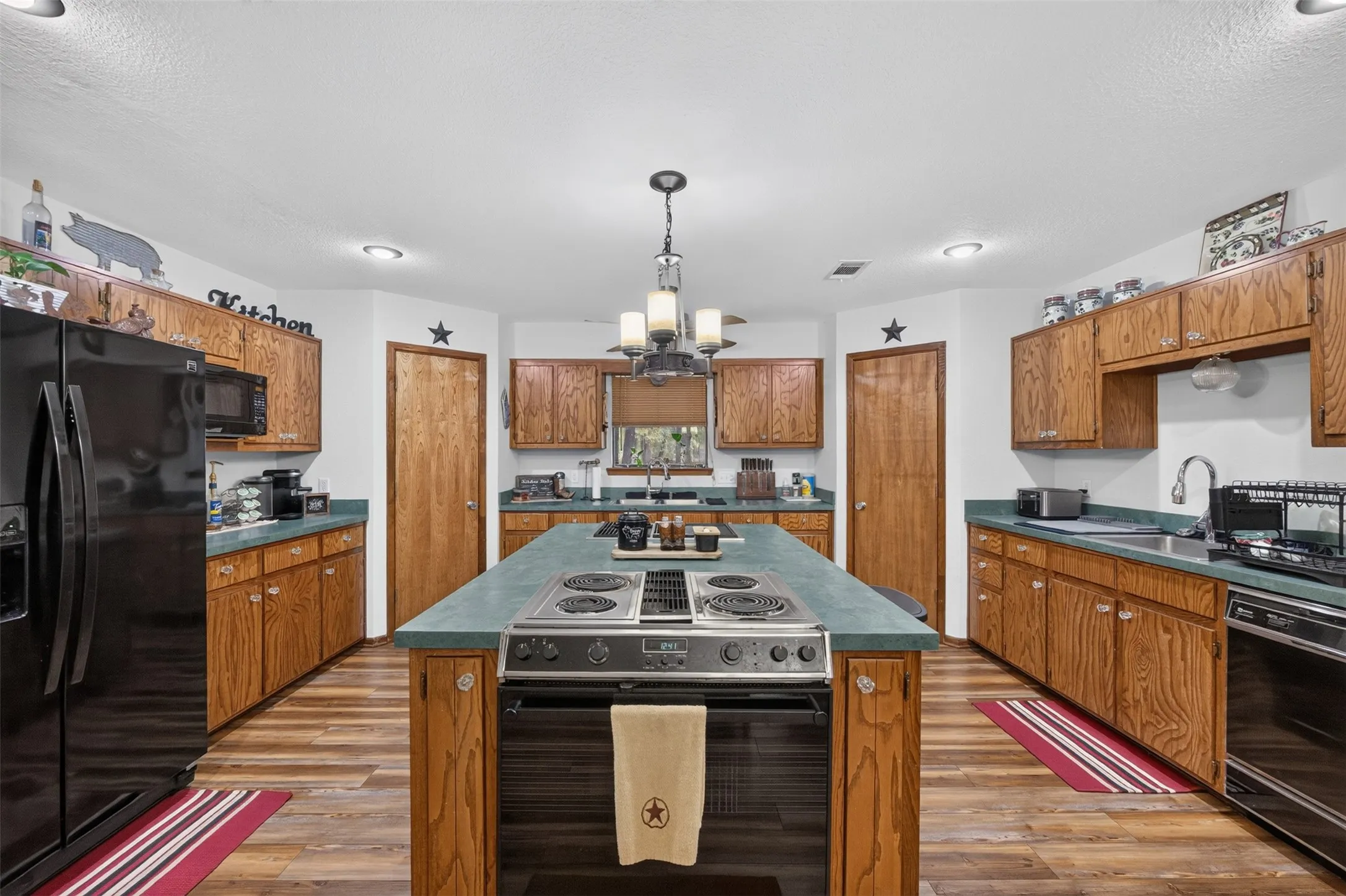 Expansive kitchen featuring wood-finish flooring, abundant wood cabinetry, a central island with built-in cooktop, and a double basin sink