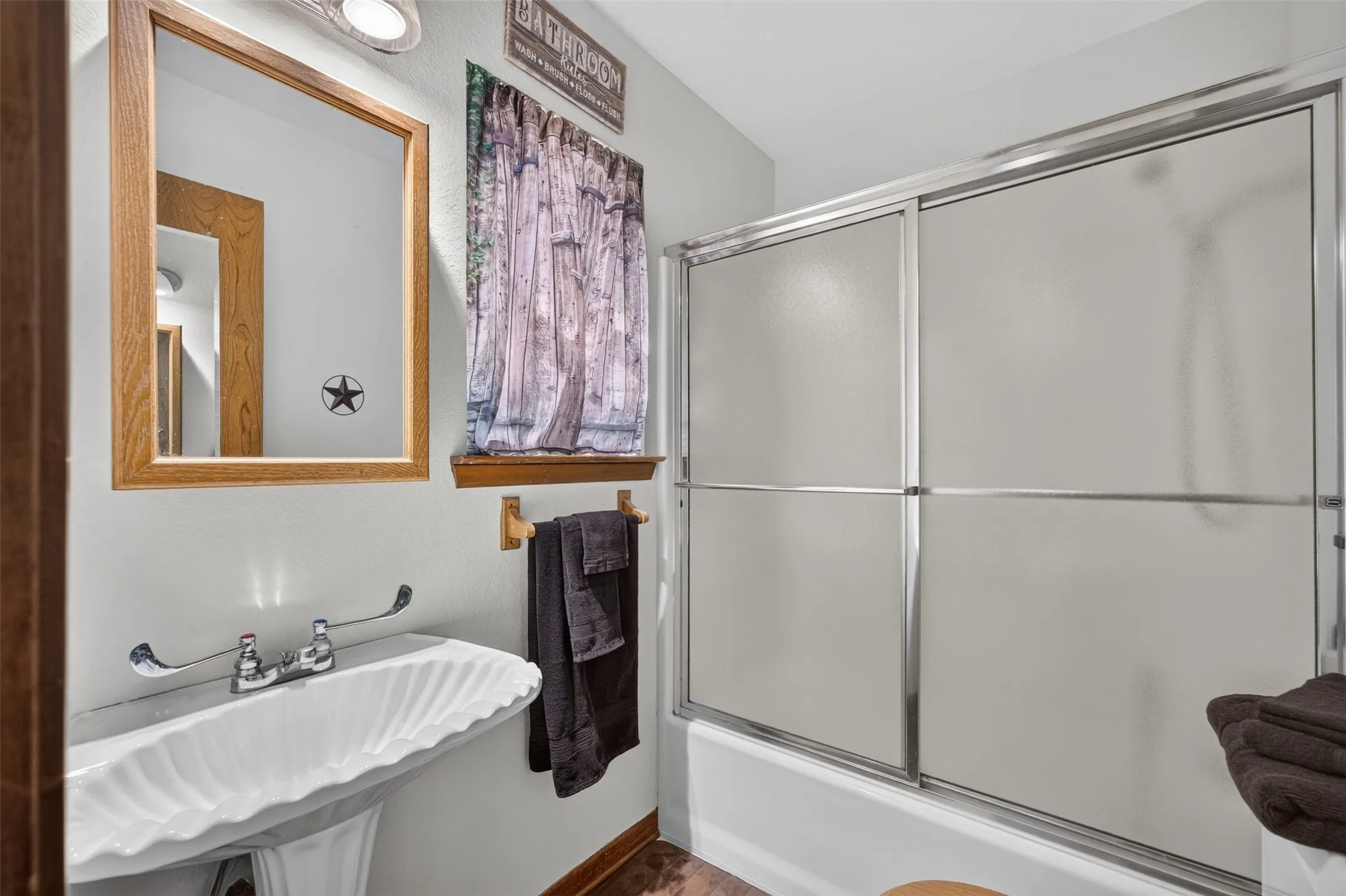 Pedestal sink with fluted basin, framed mirror, and sliding glass shower enclosure