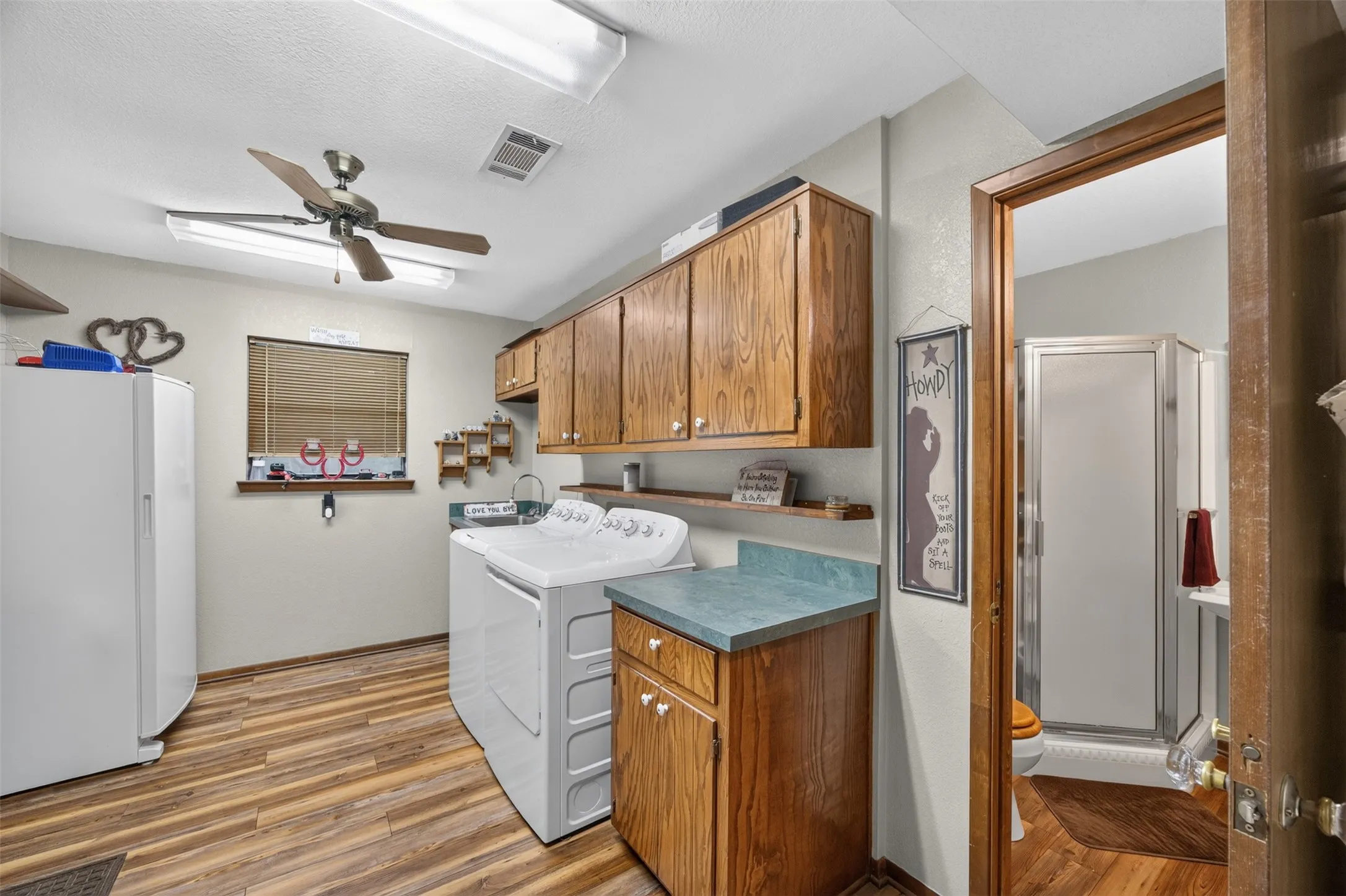 Wood-finish flooring throughout, ceiling fan with integrated lighting, and wood cabinetry offering ample storage