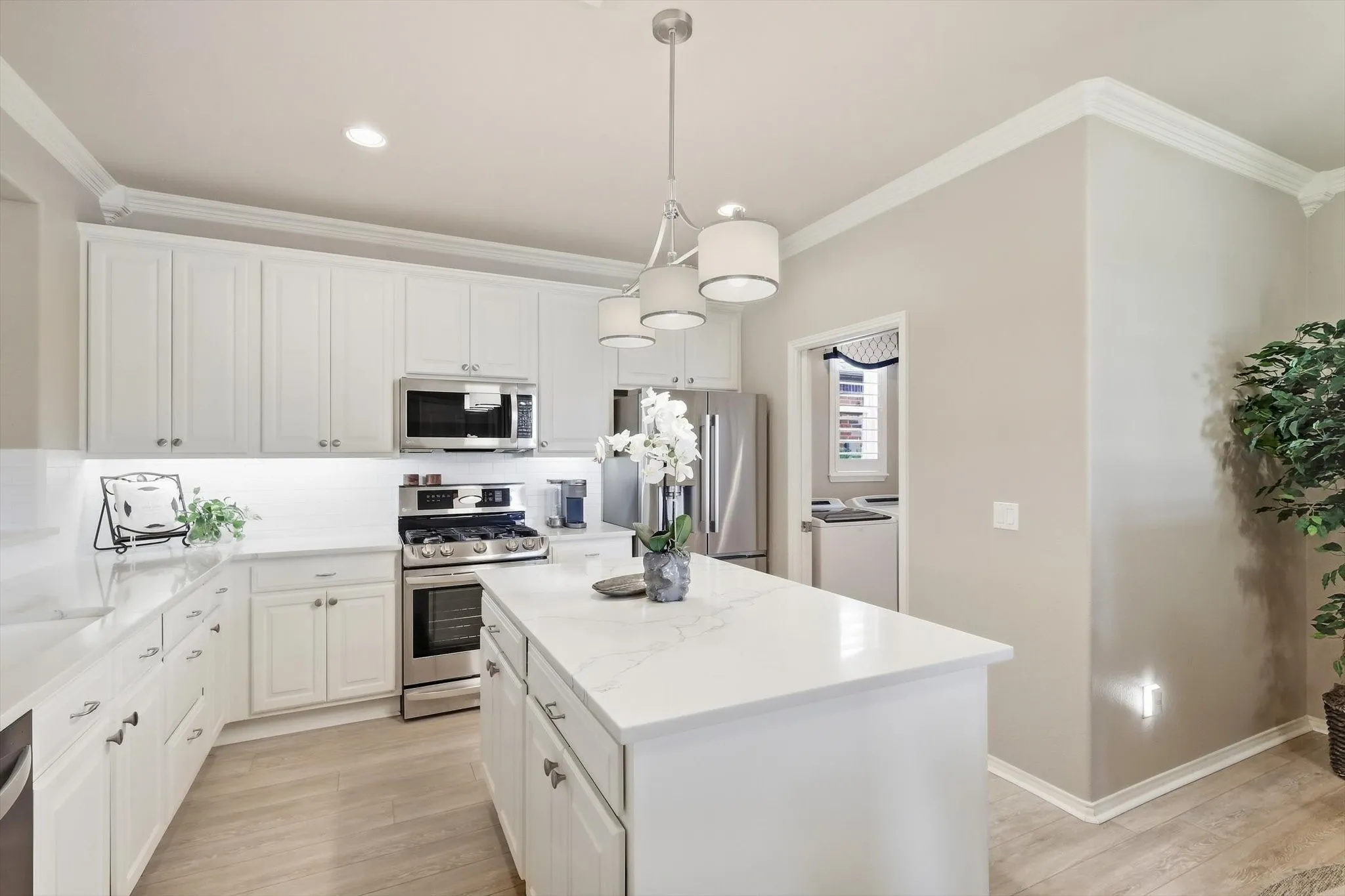 Kitchen featuring white cabinetry, light-toned countertops, stainless steel appliances, a center island, wood-finish flooring and entry to Utility Room