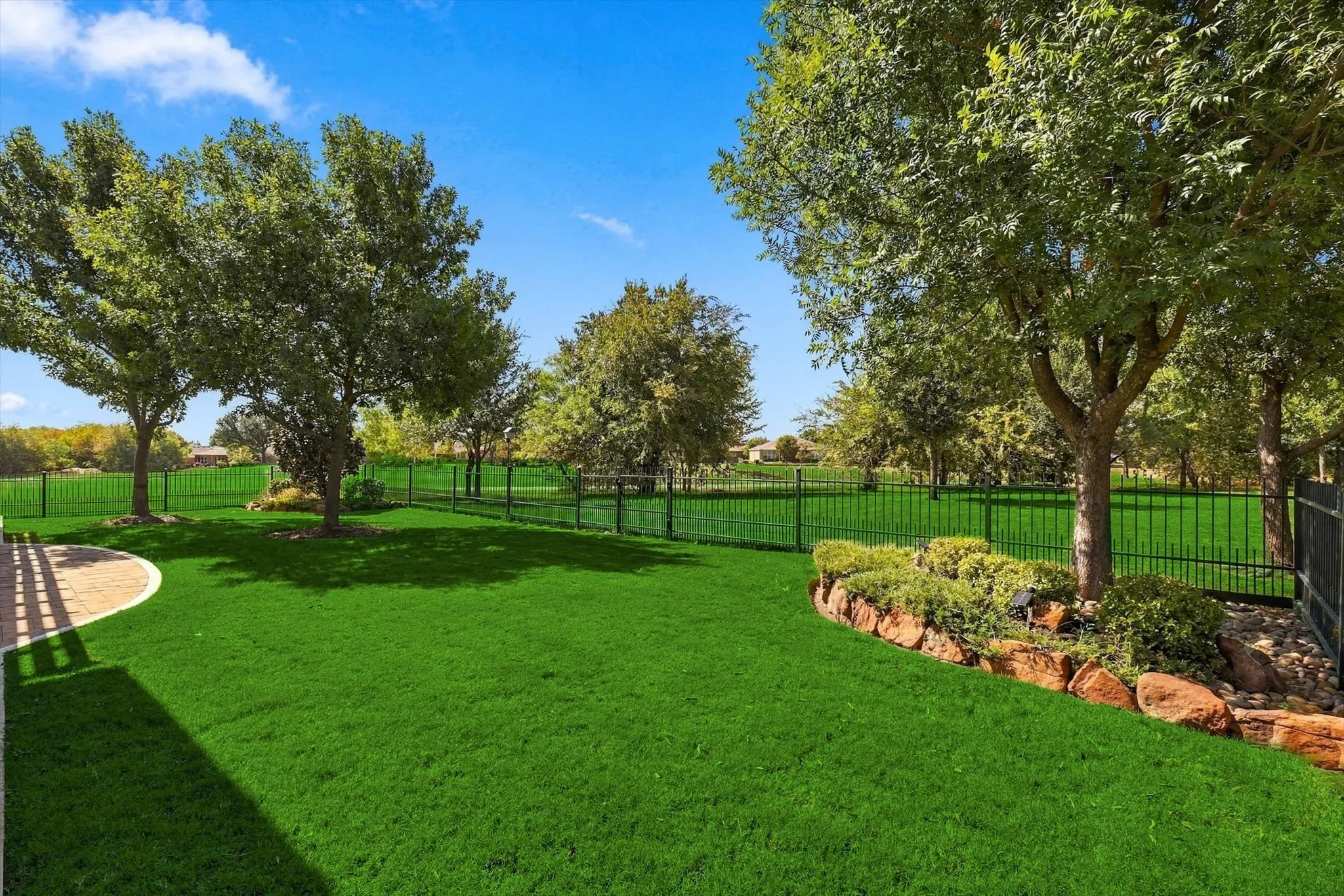 Green lawn with a view of Greenbelt, a stone-edged garden bed, and a fully fenced back yard with wrought-iron fence