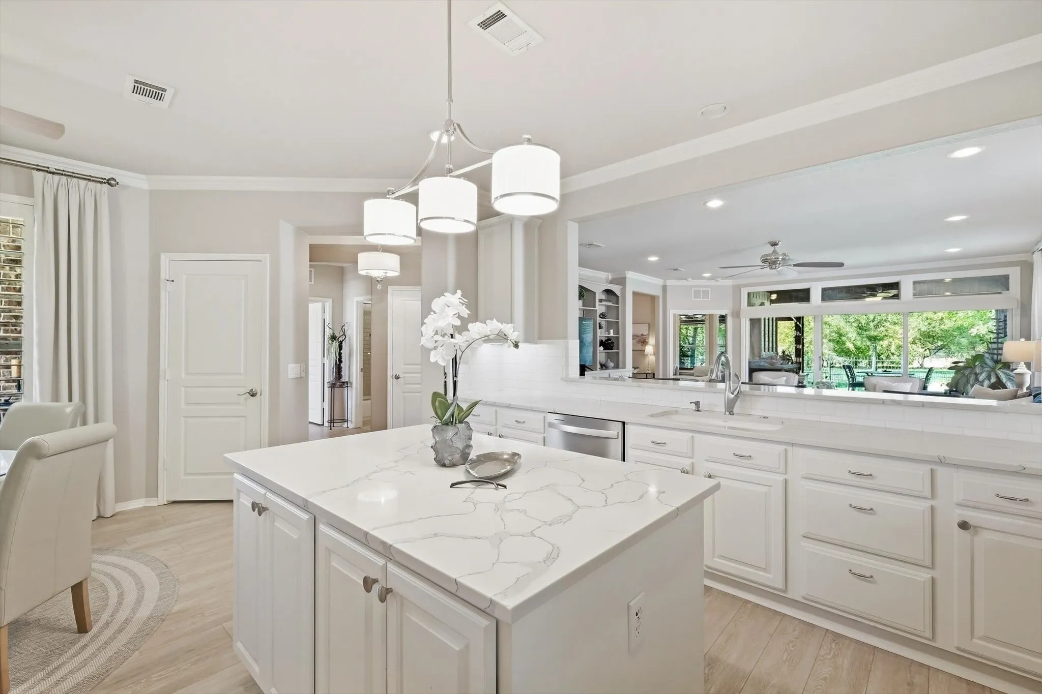 Bright, open kitchen featuring a large center island with white cabinetry, white quartz countertops, stainless steel appliances, pendant lighting, and abundant natural light from expansive windows