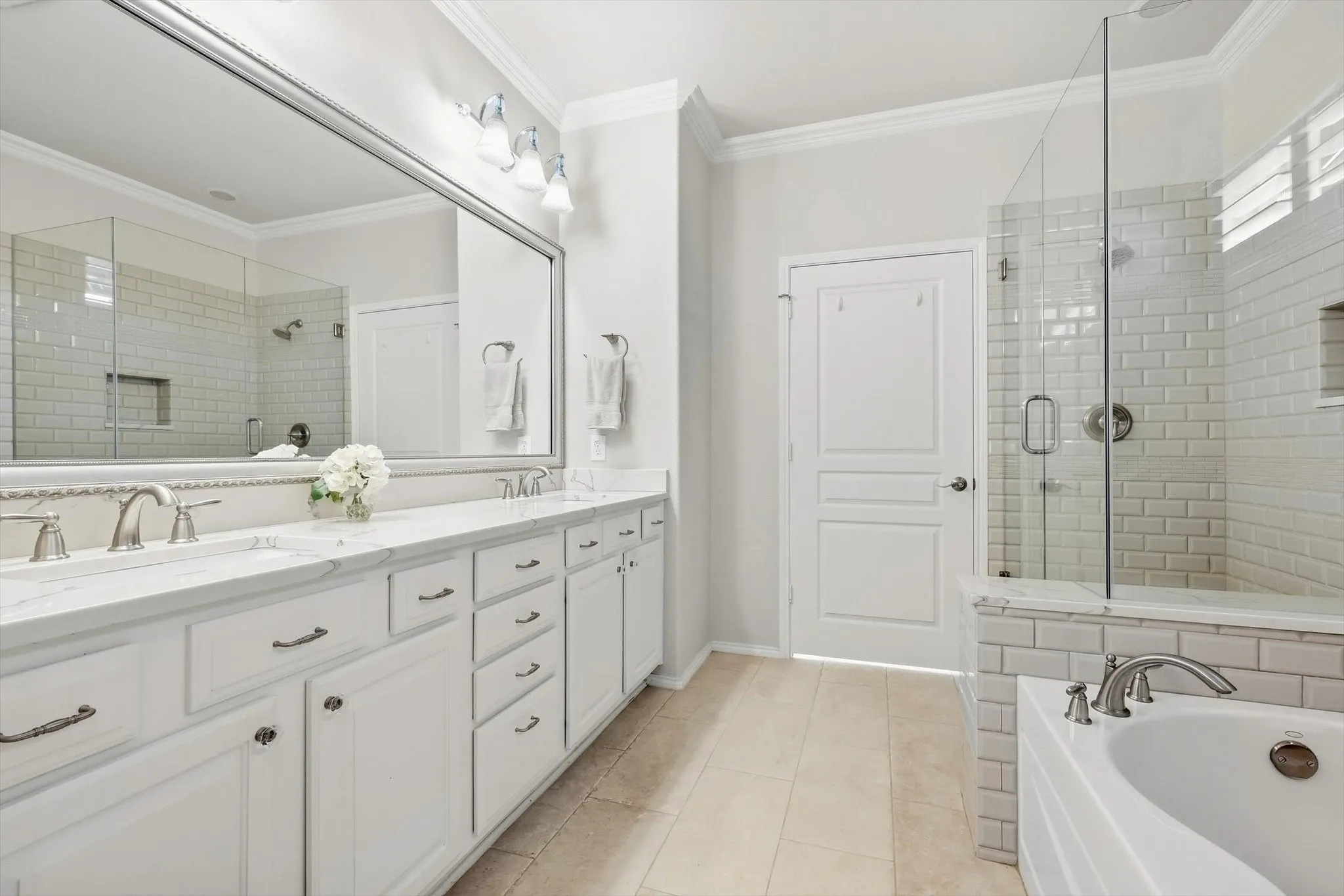Dual vanity with undermount sinks and white shaker-style cabinetry, a spacious mirror, a glass-enclosed shower with subway tile, and a built-in tub