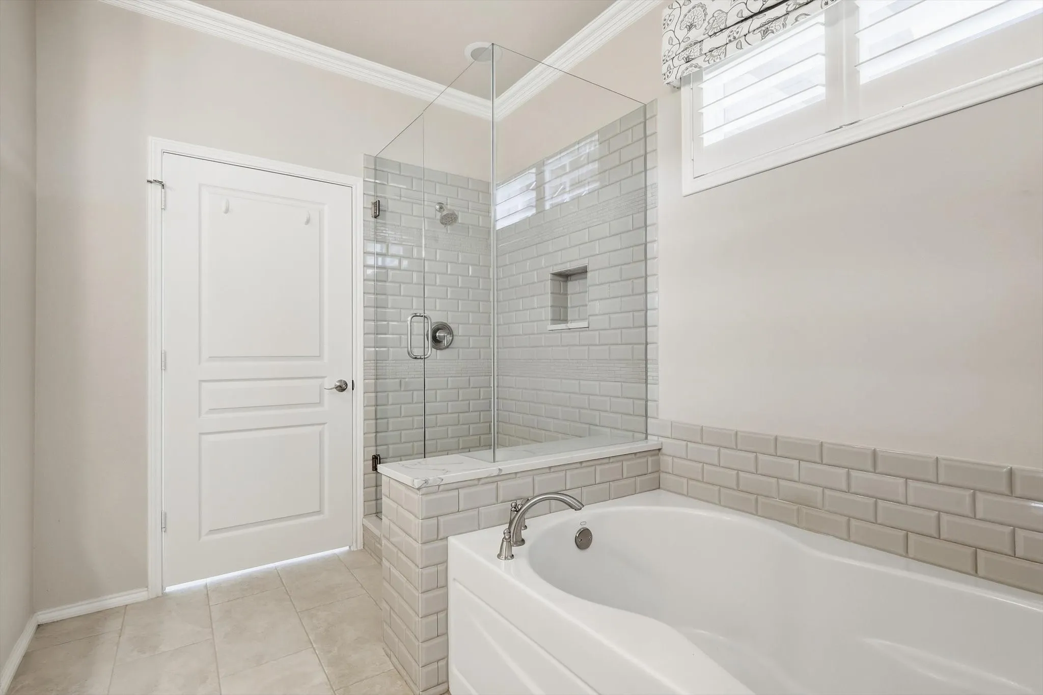Walk in glass shower enclosure, recessed shower niche, subway tile accents, soaker tub, and tile flooring